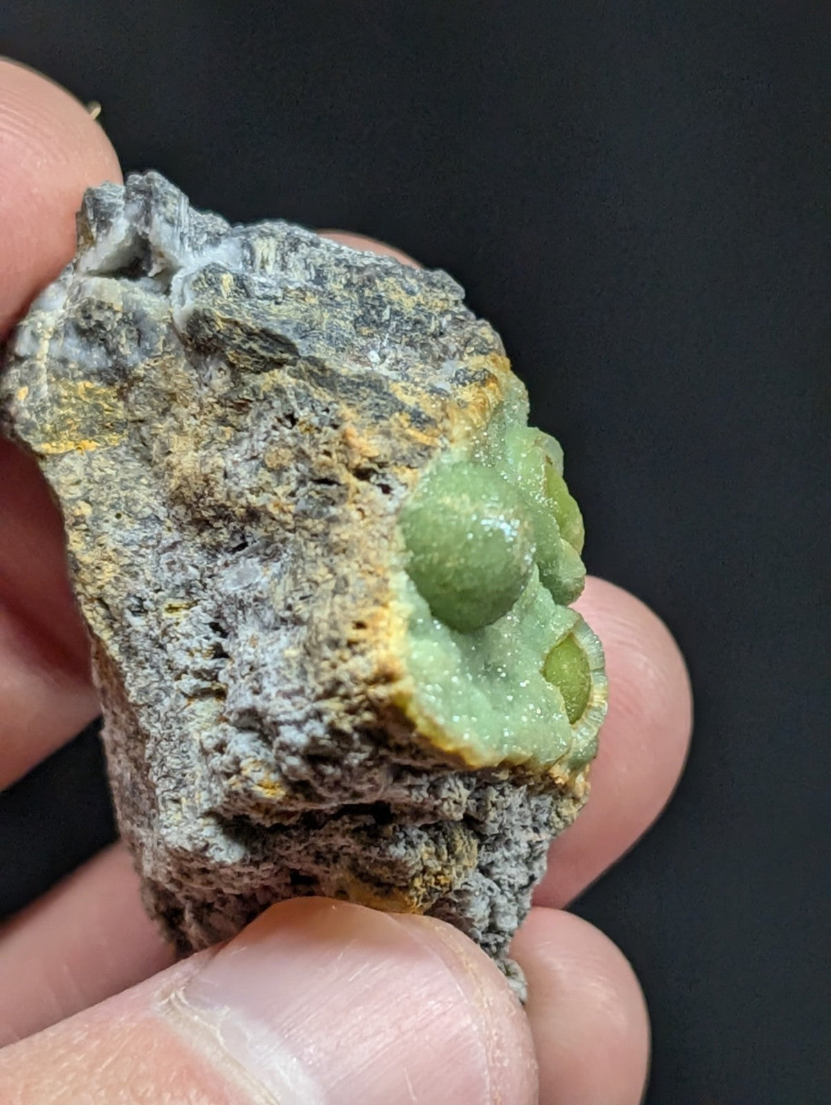 A vibrant green, translucent crystal formation nestled within a rugged gray and yellow mineral matrix.