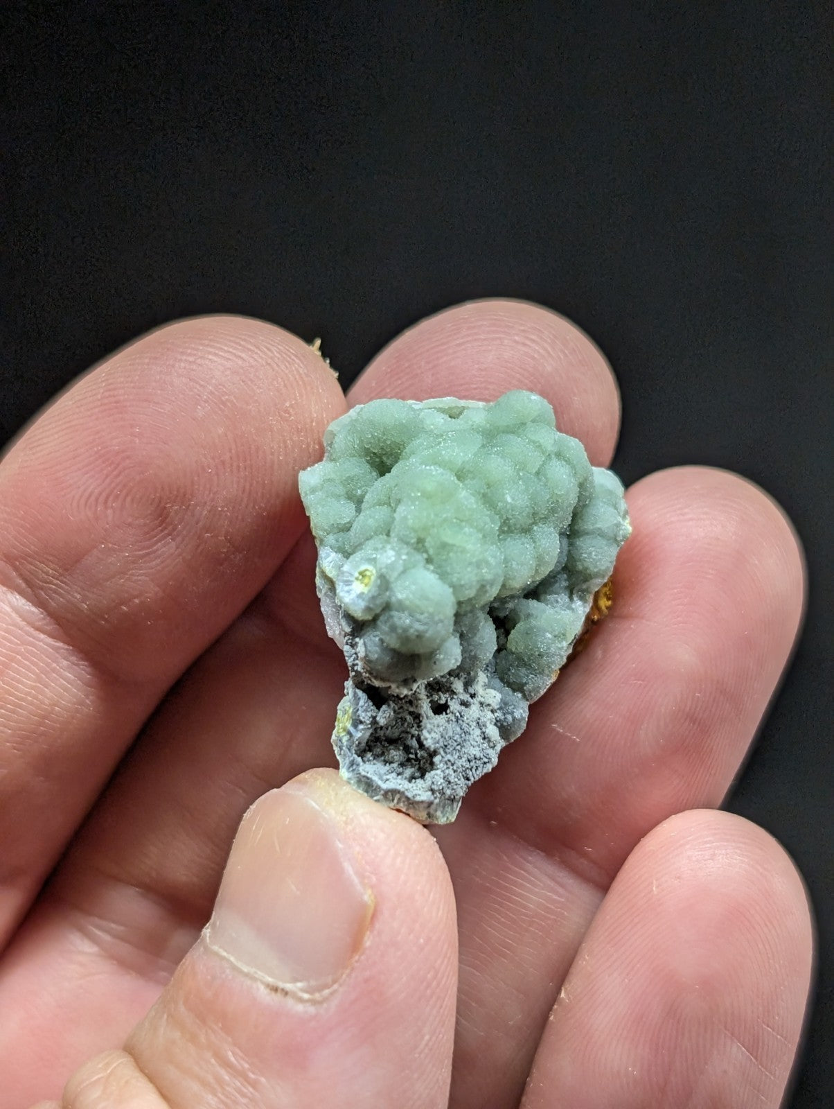 A delicate, light green mineral specimen with a textured, bumpy surface and subtle yellowish highlights.