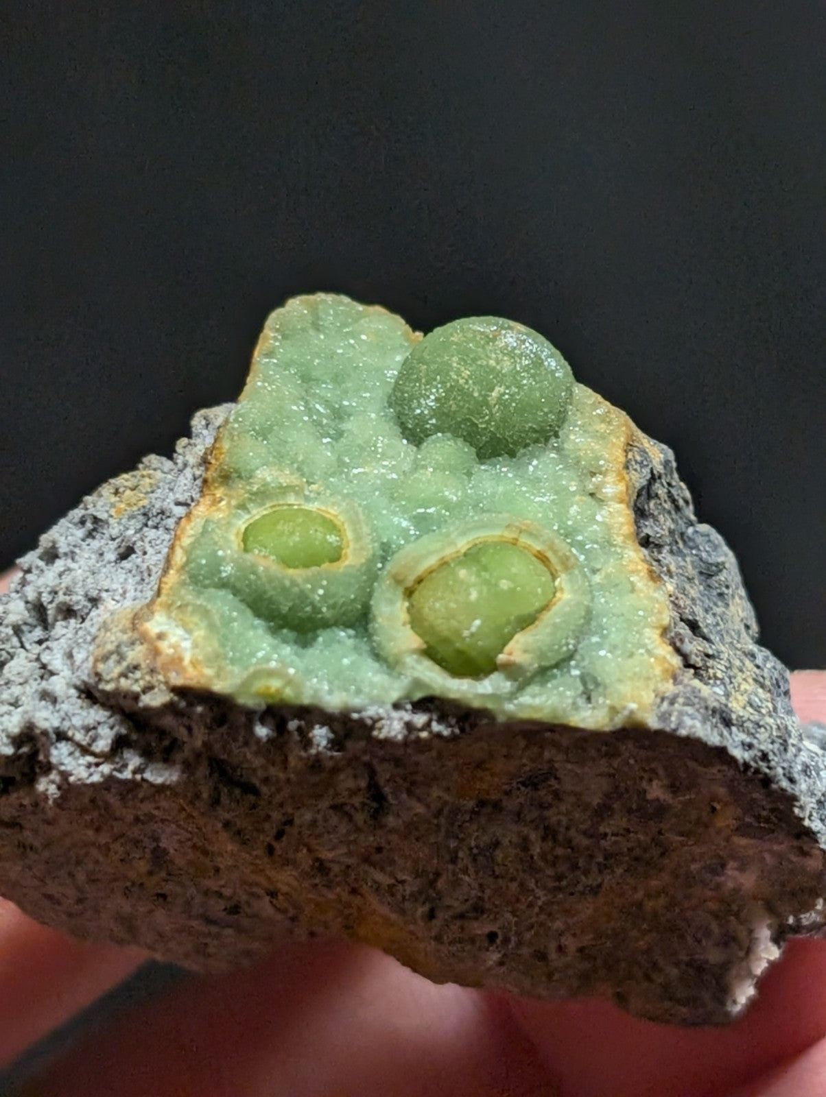 A green, crystalline mineral specimen with three rounded, translucent orbs embedded in a textured matrix.