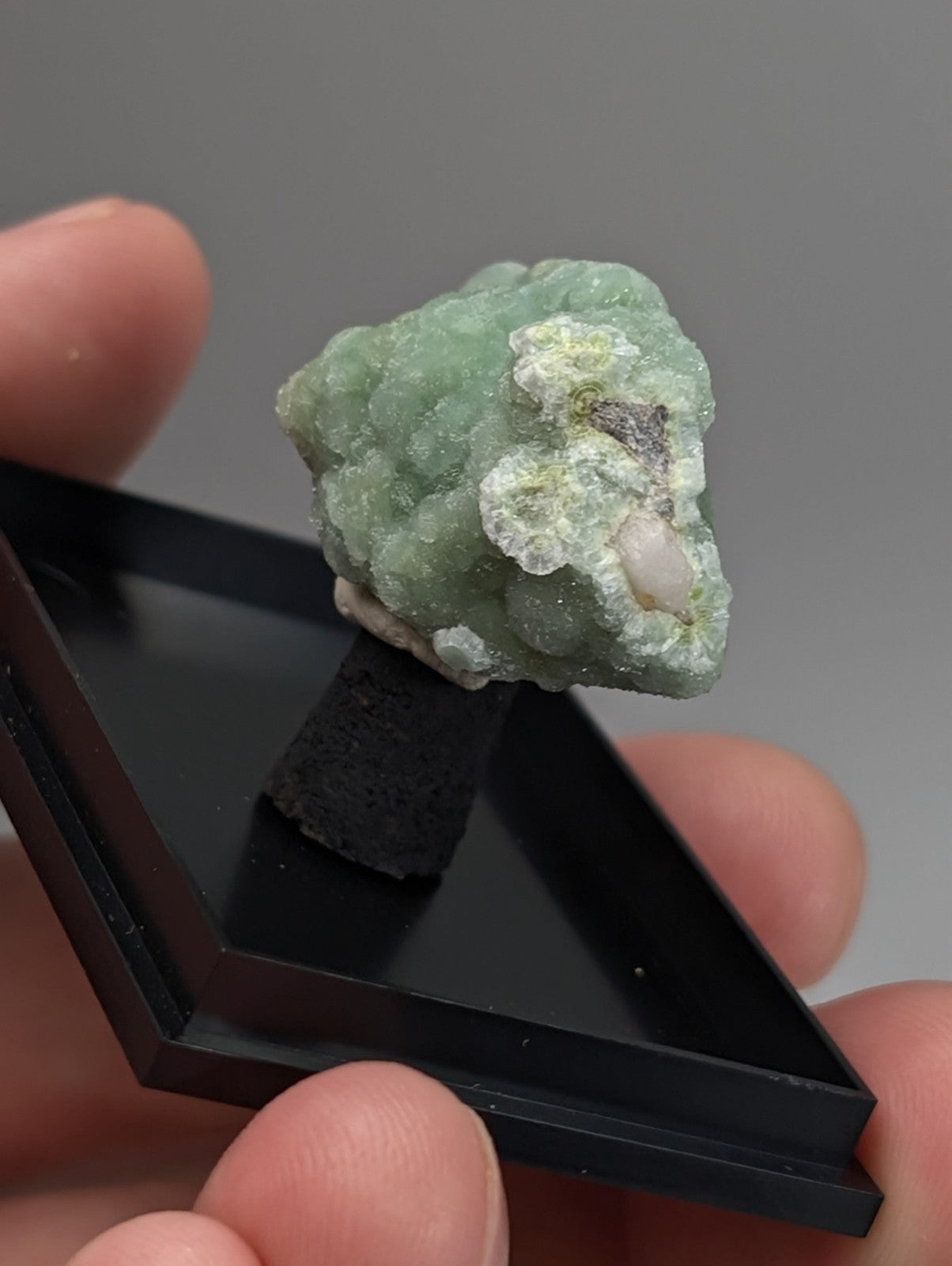Green wavellite mineral specimen with pale green texture and white pinkish inclusions on black stand from arkansas usa