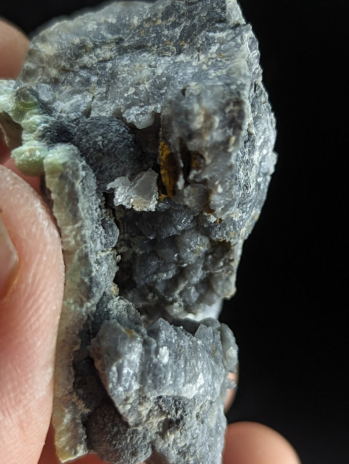 A rugged, grayish-green mineral specimen with a rough, crystalline texture and embedded darker inclusions.