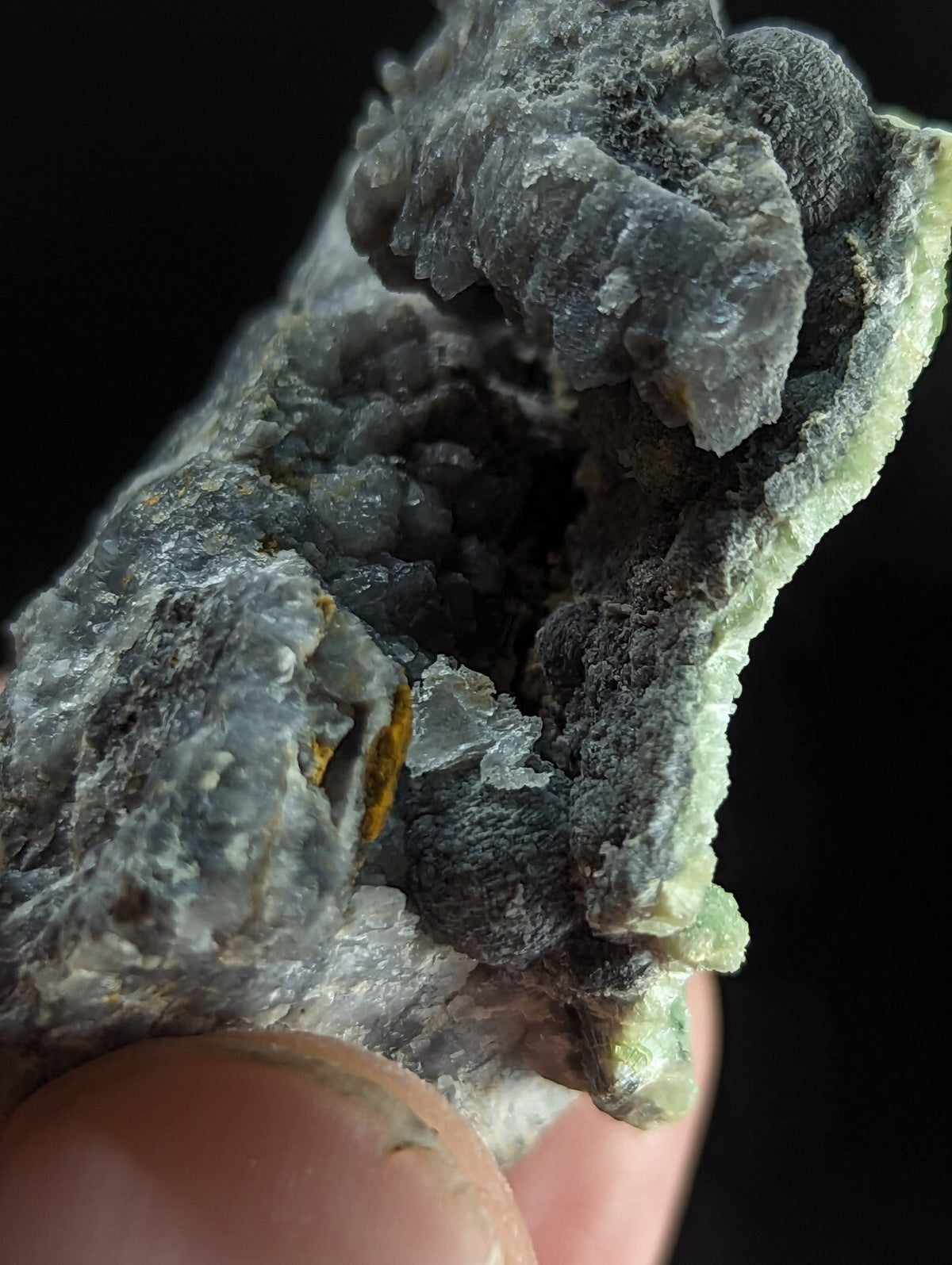 A rugged, gray-green mineral specimen with crystalline formations and a rough, textured surface.