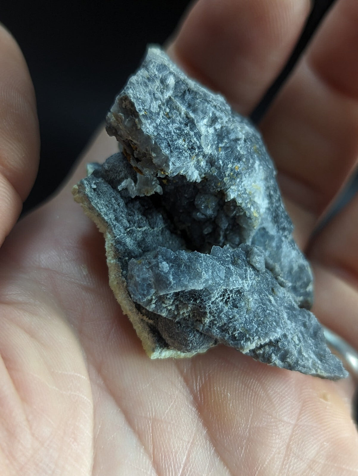 A rough, grayish-blue mineral specimen with a crystalline interior and textured surface.