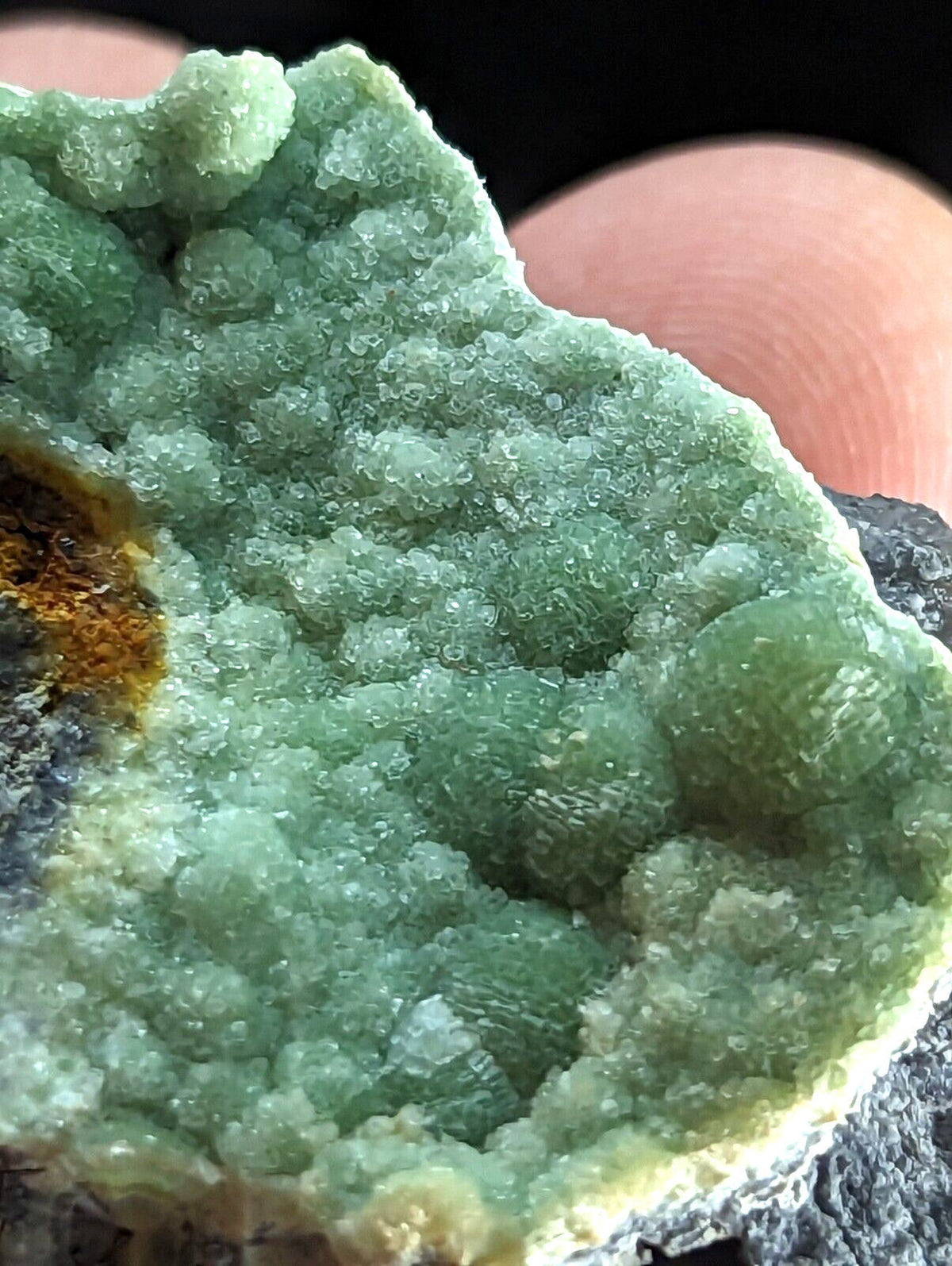 A vibrant green, crystalline mineral specimen with a textured surface and subtle yellowish-orange inclusions.