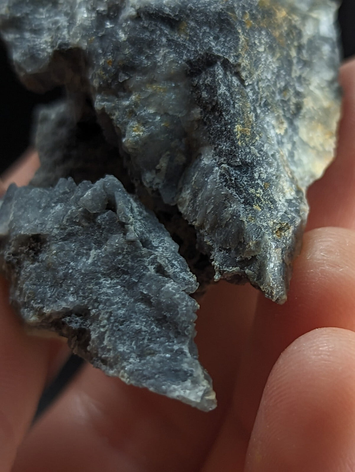 A rough, jagged piece of dark gray rock with subtle yellowish mineral veins and a textured, uneven surface.