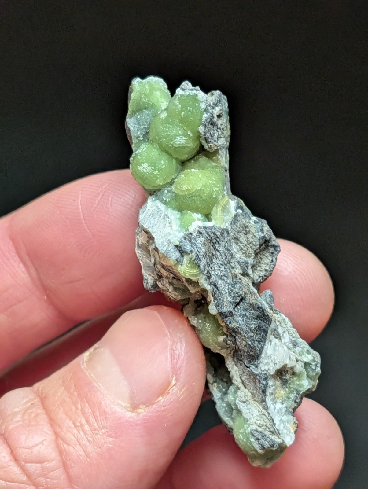 A cluster of vibrant green, translucent crystals nestled within a rough, grayish matrix rock.
