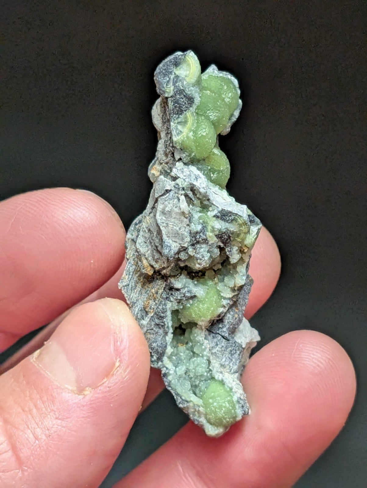 A cluster of vibrant green, translucent crystals growing from a rough gray rock matrix.