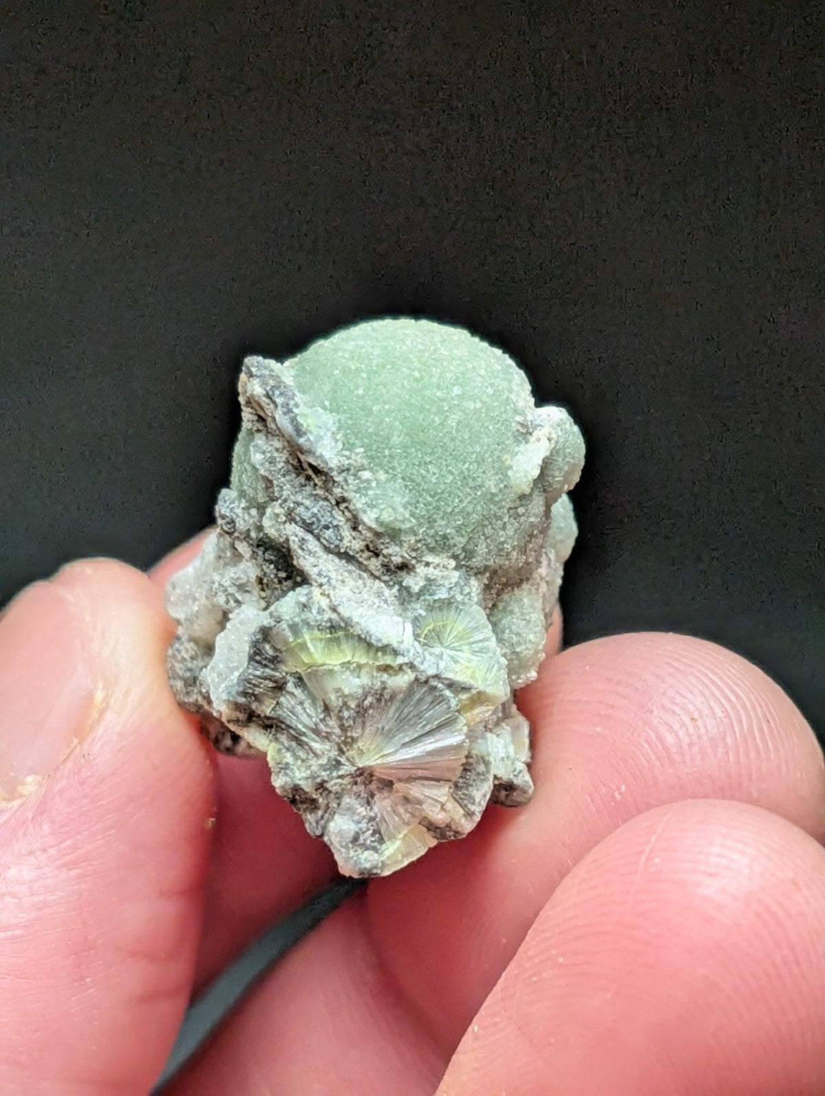 A pale green, rounded mineral specimen with a rough, textured surface and embedded crystalline formations.