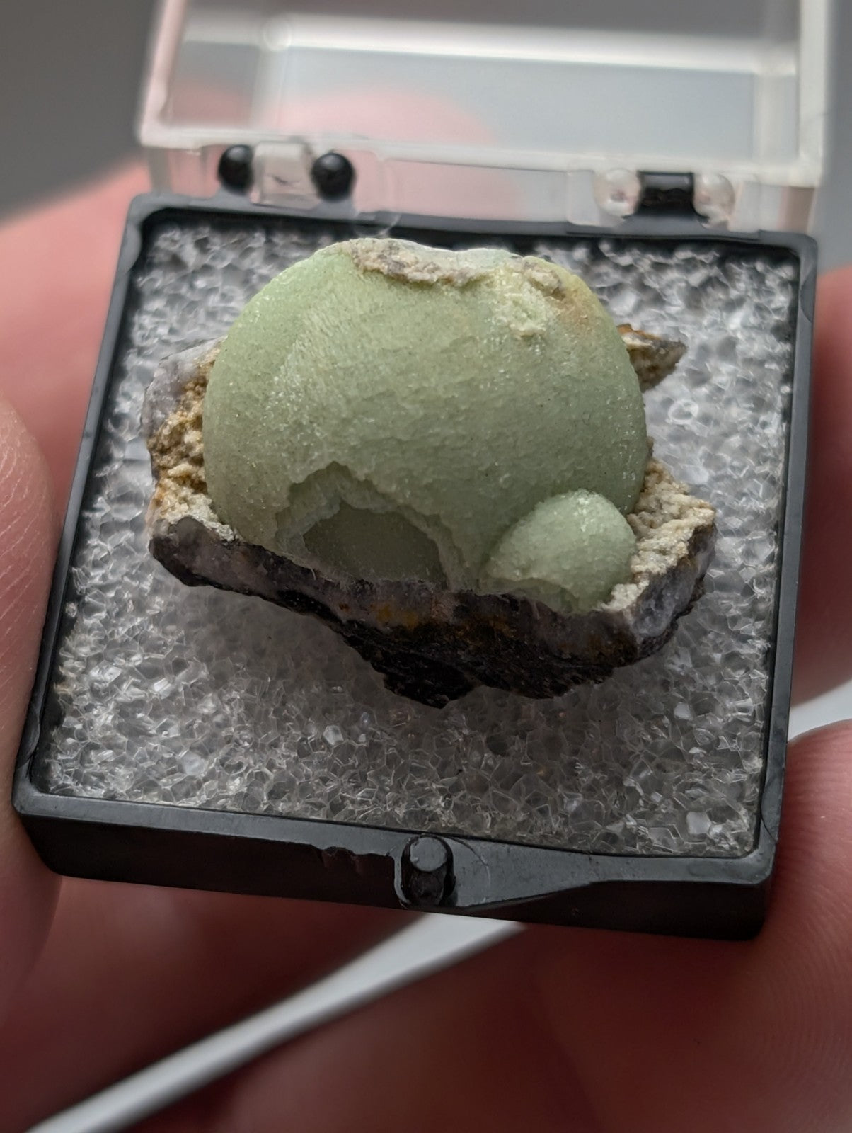 A pale green rounded green wavellite geode with rough crystalline exterior and smooth interior in black display case from Mauldin Mountain Arkansas