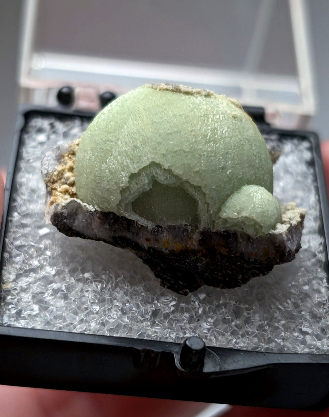 A pale green spherical wavellite geode with cracked crystalline surface and dark mineral base from Mauldin Mountain Arkansas