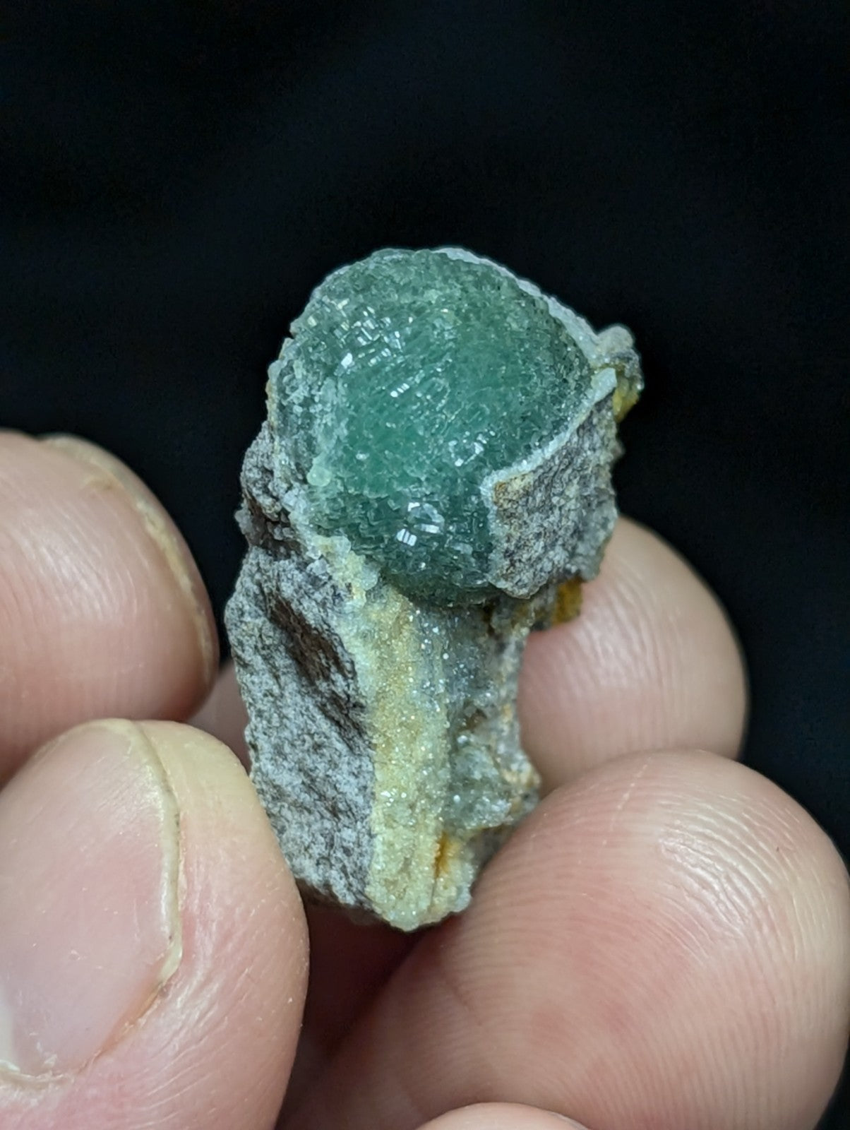 A translucent green fluorite crystal nestled in a rough, grayish matrix with subtle yellow streaks.