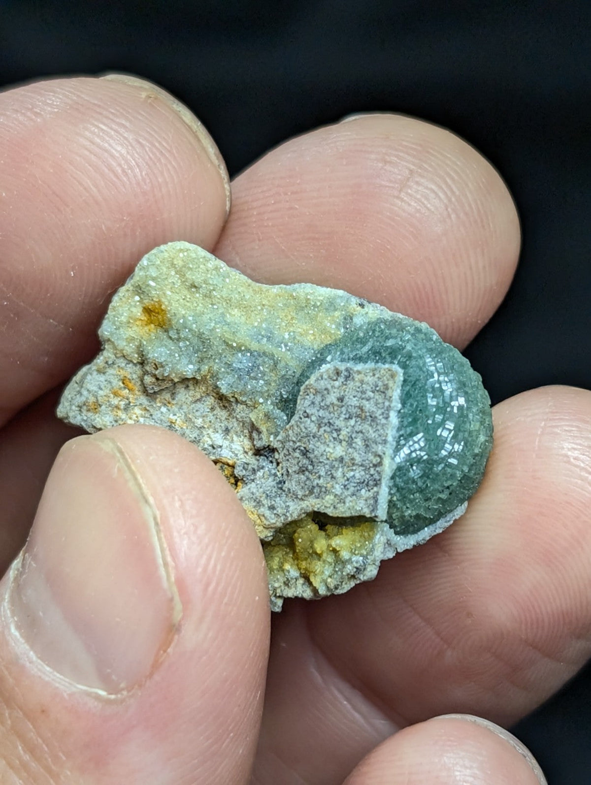 A rough, irregularly shaped mineral specimen with a mix of greenish-blue and yellow-orange hues, featuring crystalline textures and natural rock matrix.