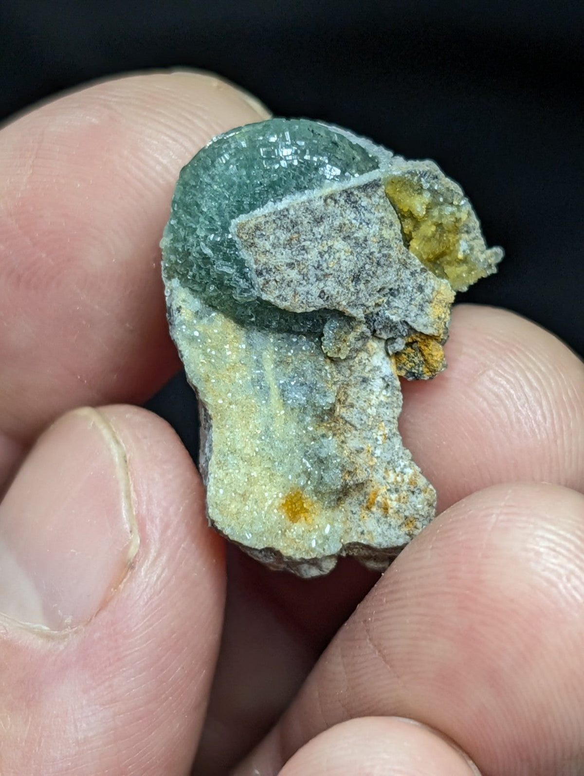 A rough, irregularly shaped mineral specimen with a greenish-blue upper section and patches of yellow-orange oxidation on its surface.