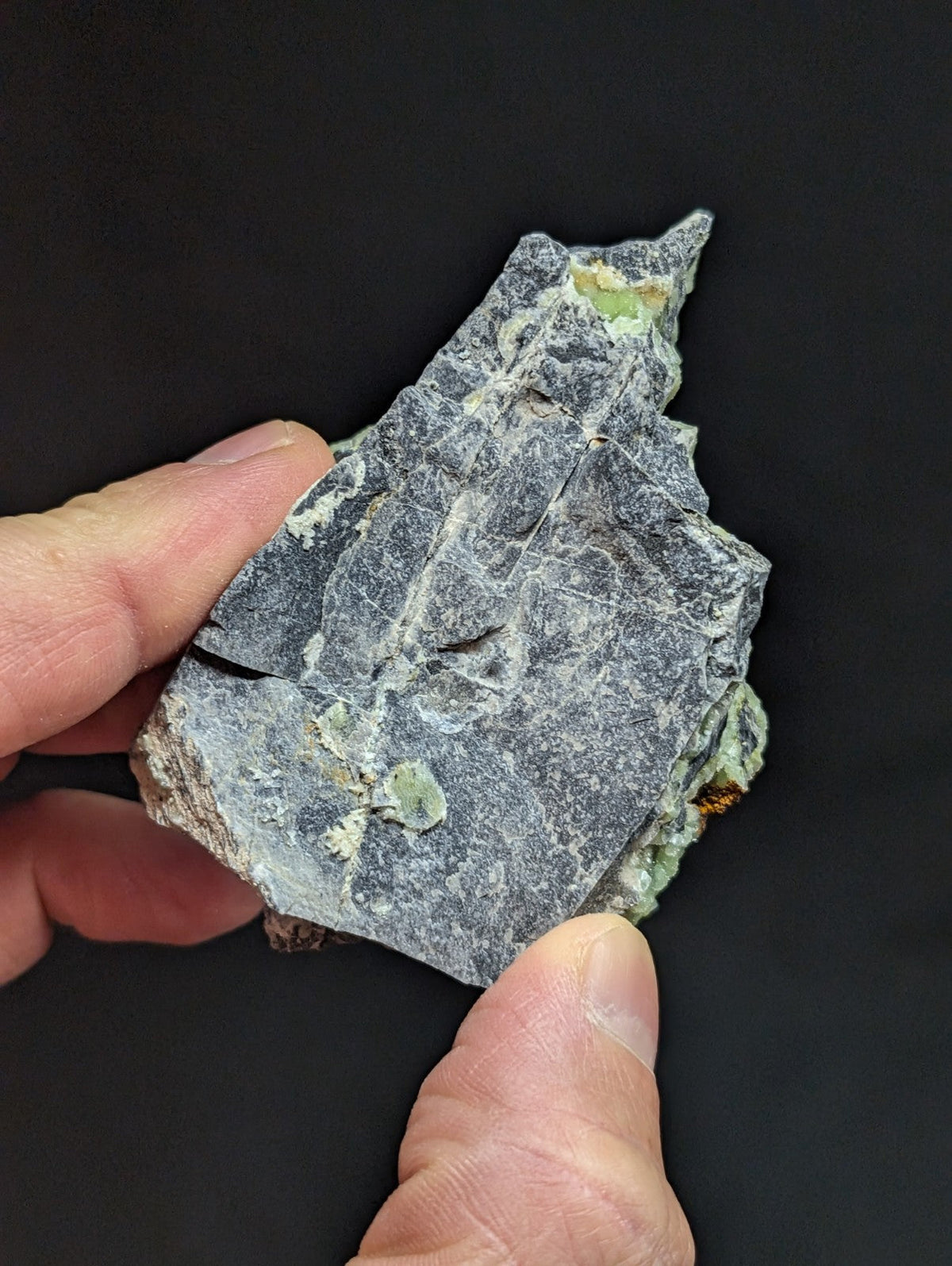 A rough, irregularly shaped gray rock with patches of green mineral inclusions.