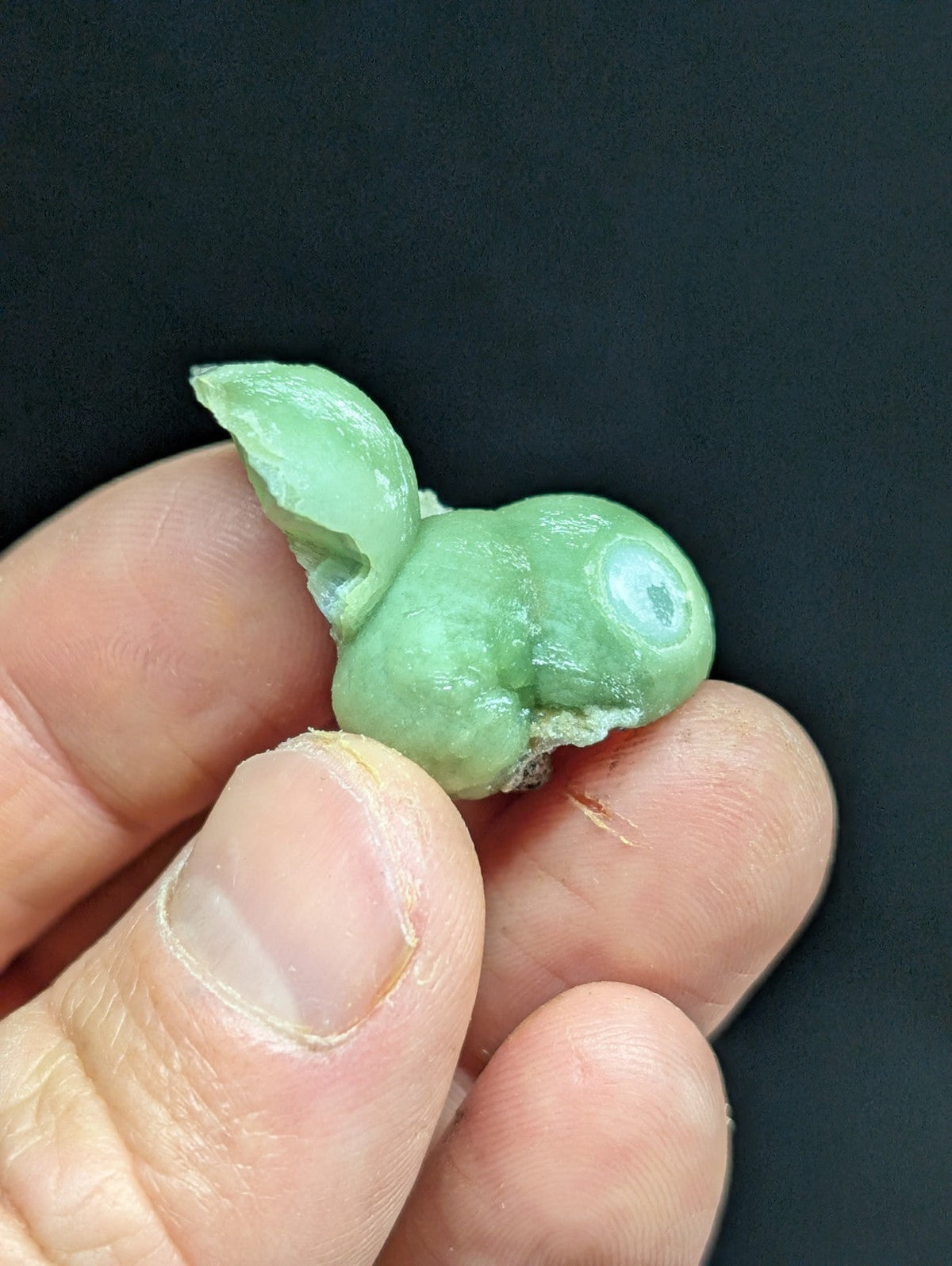 A small, light green jade figurine with a smooth, polished surface and one visible eye.