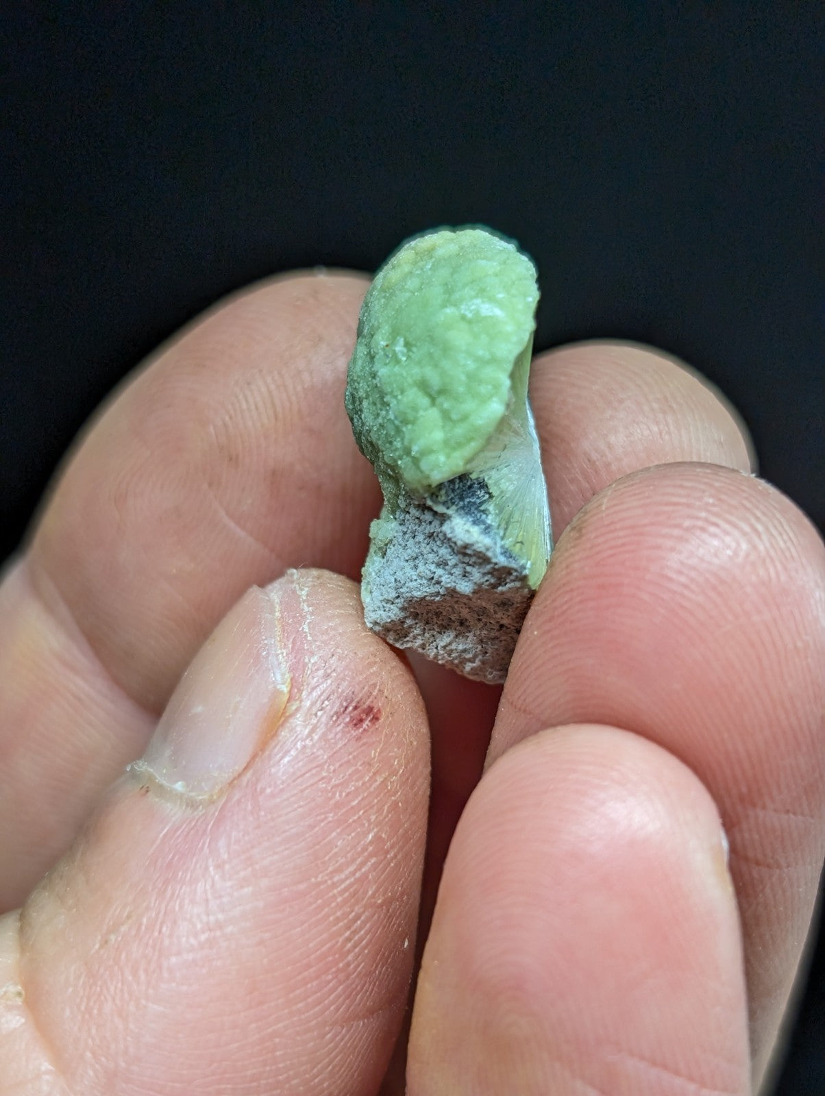 A rough, light green mineral specimen with a slightly textured surface and some grayish matrix material attached.