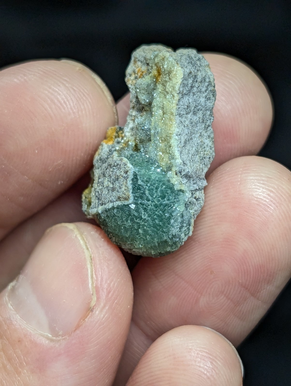 A rough, irregularly shaped green mineral specimen with a translucent quality and patches of grayish matrix material.