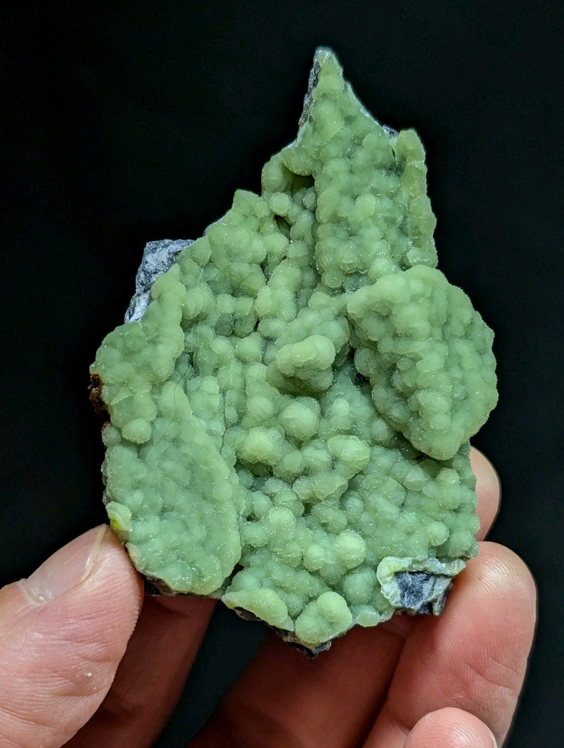 A vibrant green, textured mineral specimen with a bumpy, clustered surface and some grayish rock matrix.