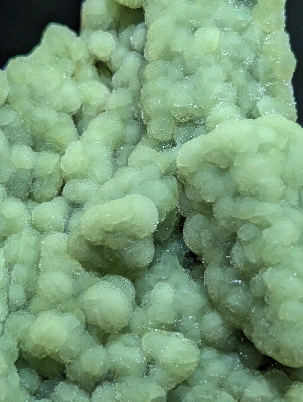 A cluster of pale green, translucent mineral crystals with a rough, bubbly texture.
