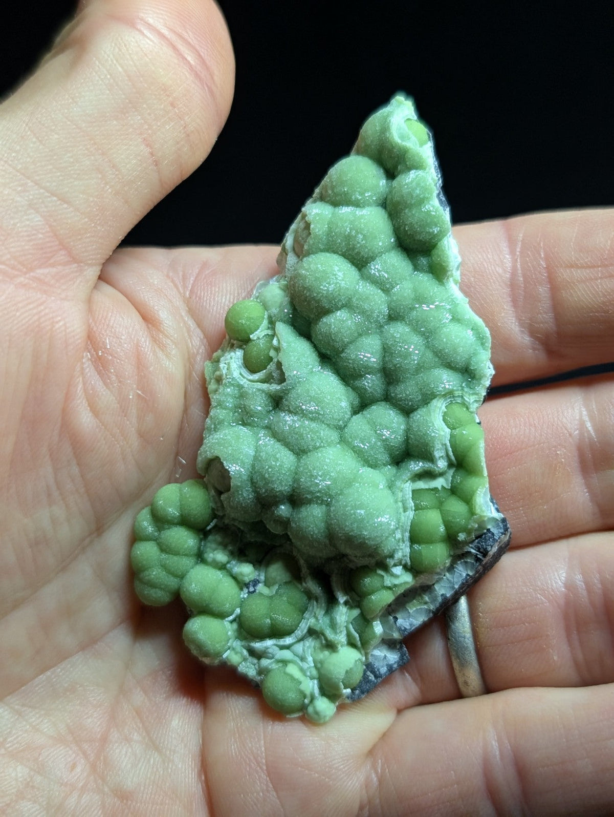 A hand holds a striking green, bumpy mineral specimen with rounded nodules and a rough-textured surface.