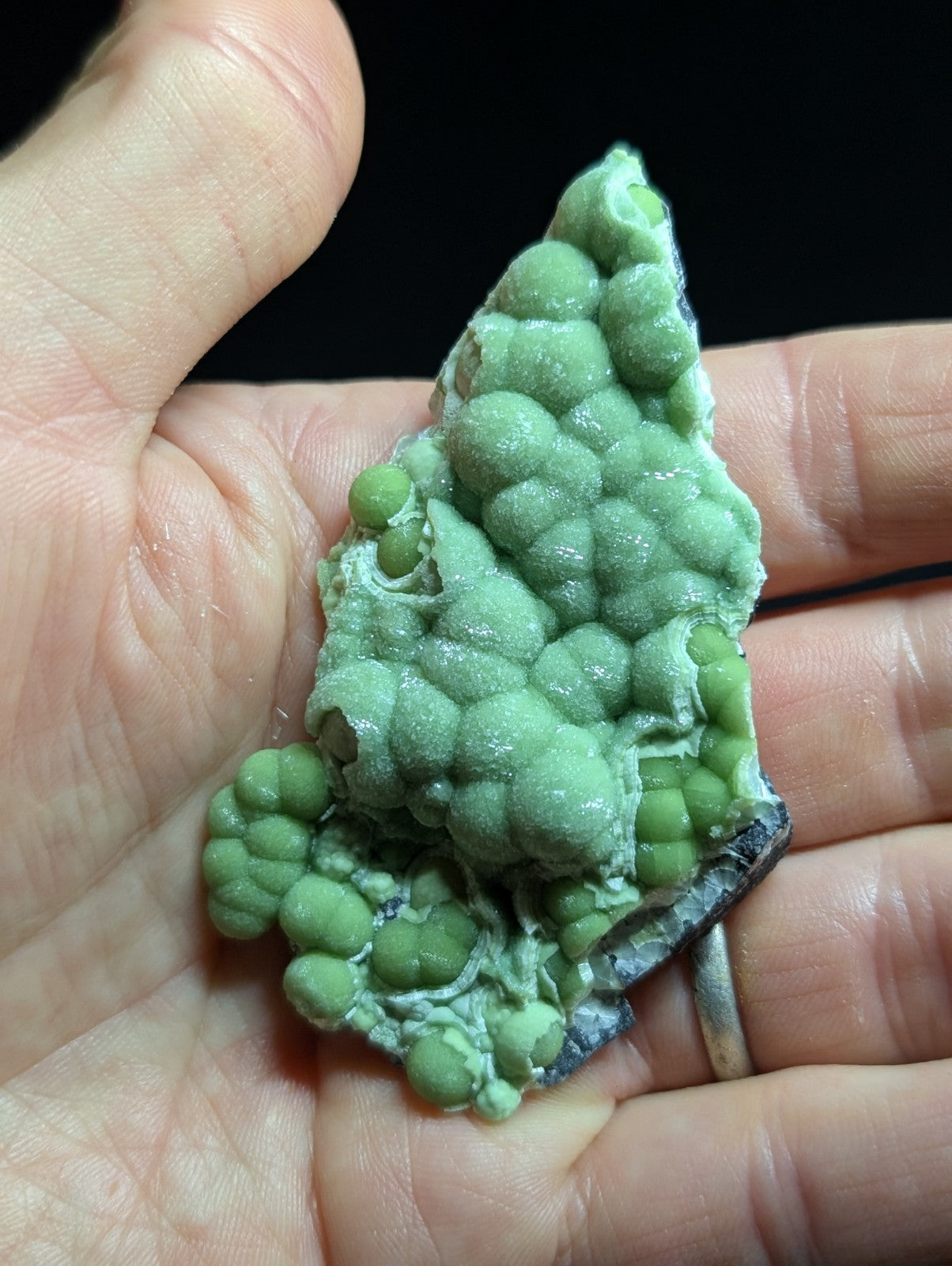 A hand holds a striking green, bumpy mineral specimen with rounded nodules and a rough-textured surface.