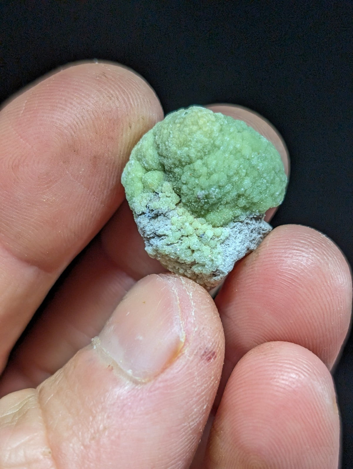 A textured, light green mineral specimen with a rough, bumpy surface and darker grayish patches.