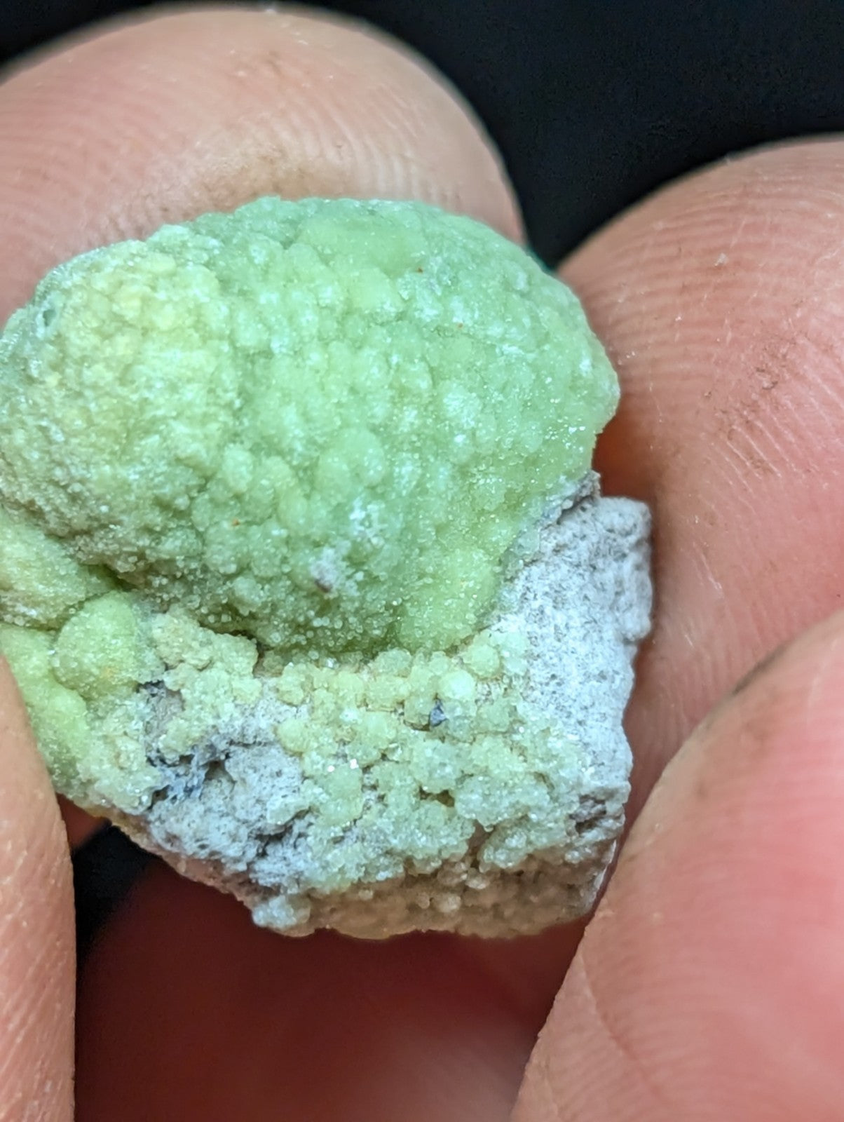 A textured, light green mineral specimen with a powdery surface and grayish patches.