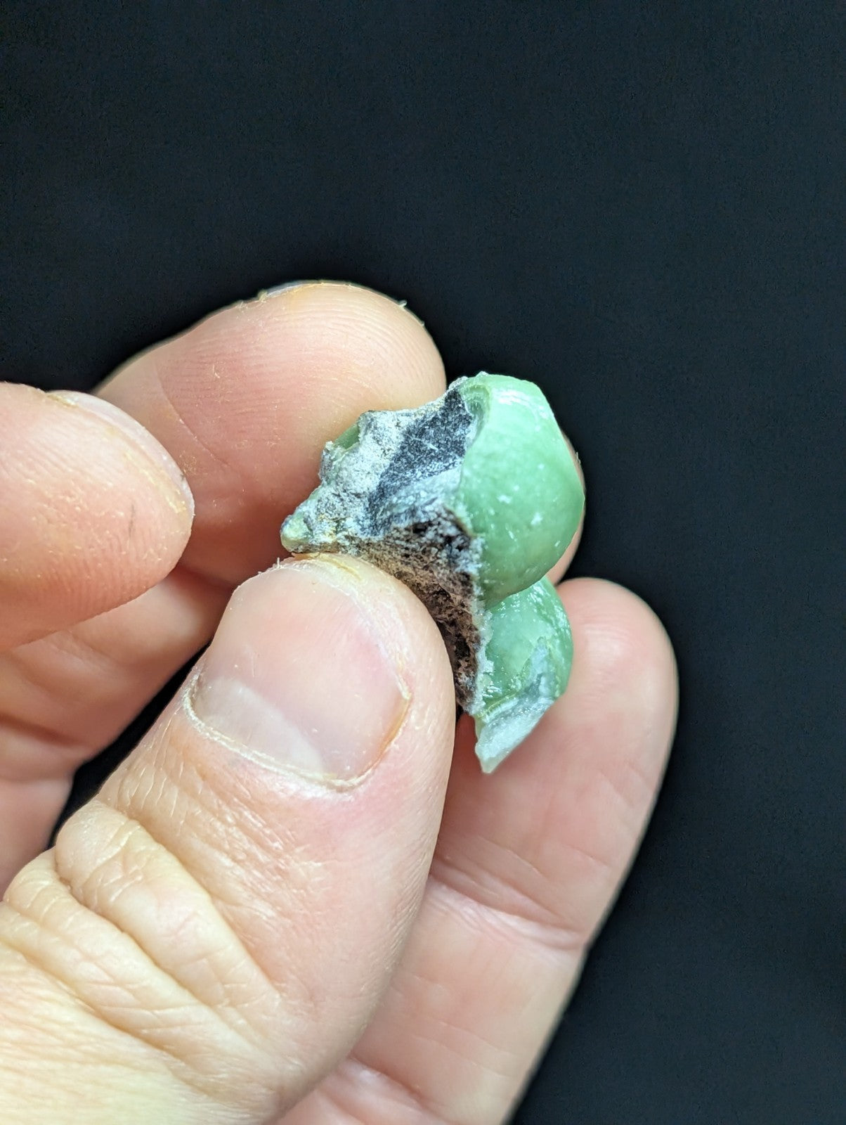 A weathered, light green jadeite bead with a rough, partially corroded surface and visible dark patina.