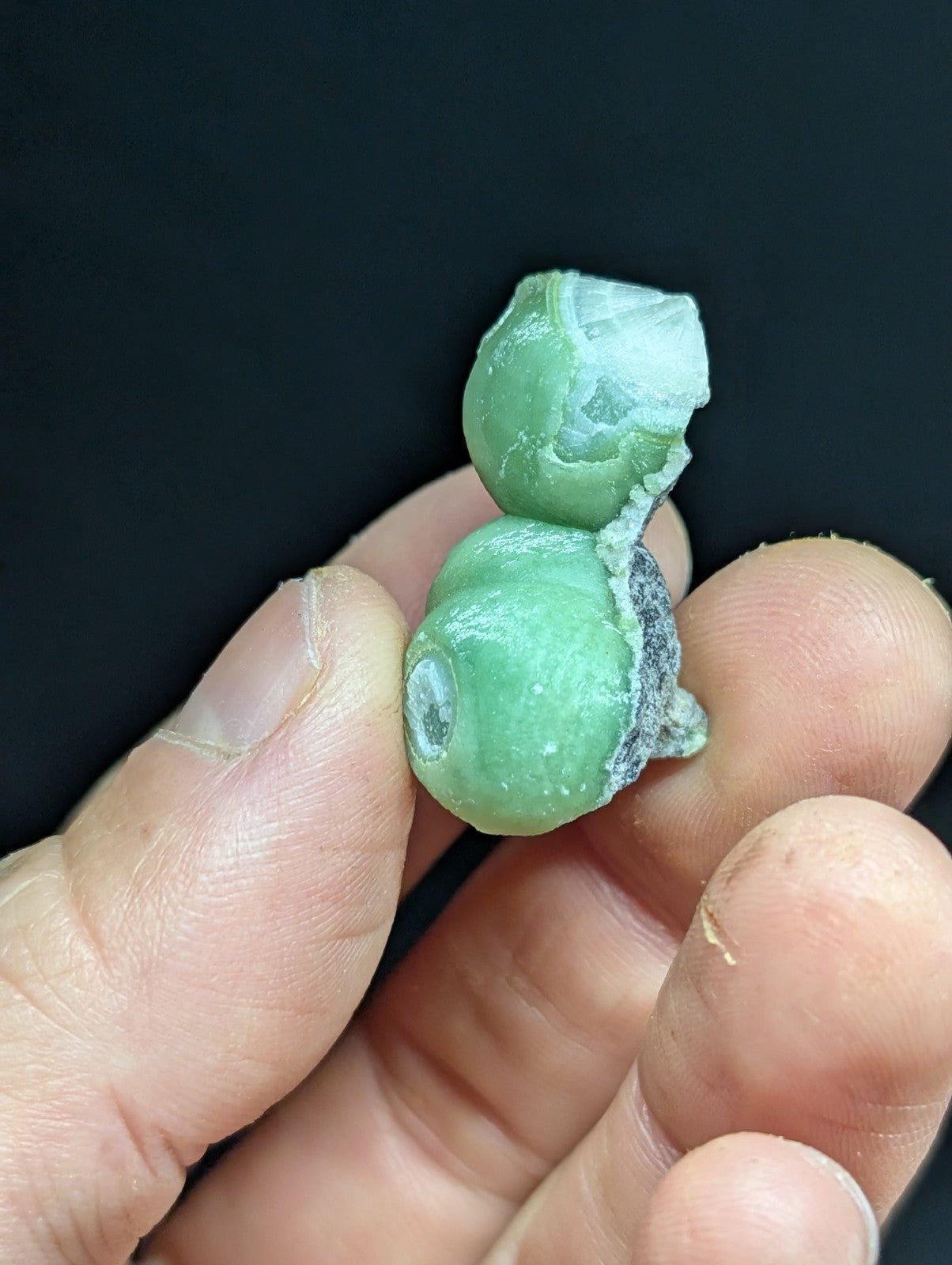 A hand holds a broken, light green jade gourd with a translucent quality and visible internal veining.
