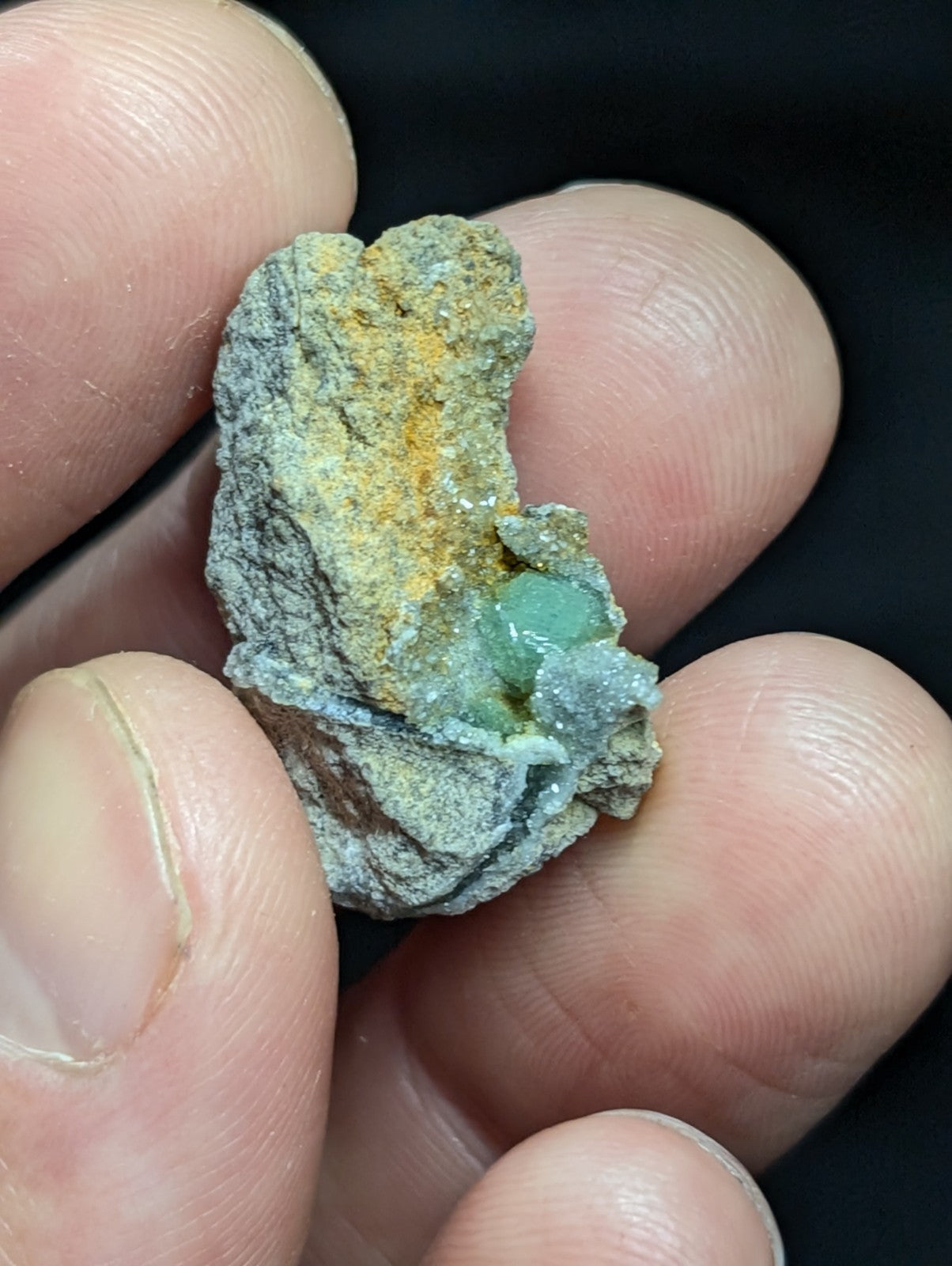 A rough, irregularly shaped mineral specimen with a grayish matrix and patches of vibrant green crystals embedded within it.