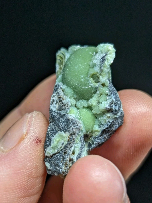 A smooth, light green spherical mineral nestled within a rough, dark gray rock matrix.