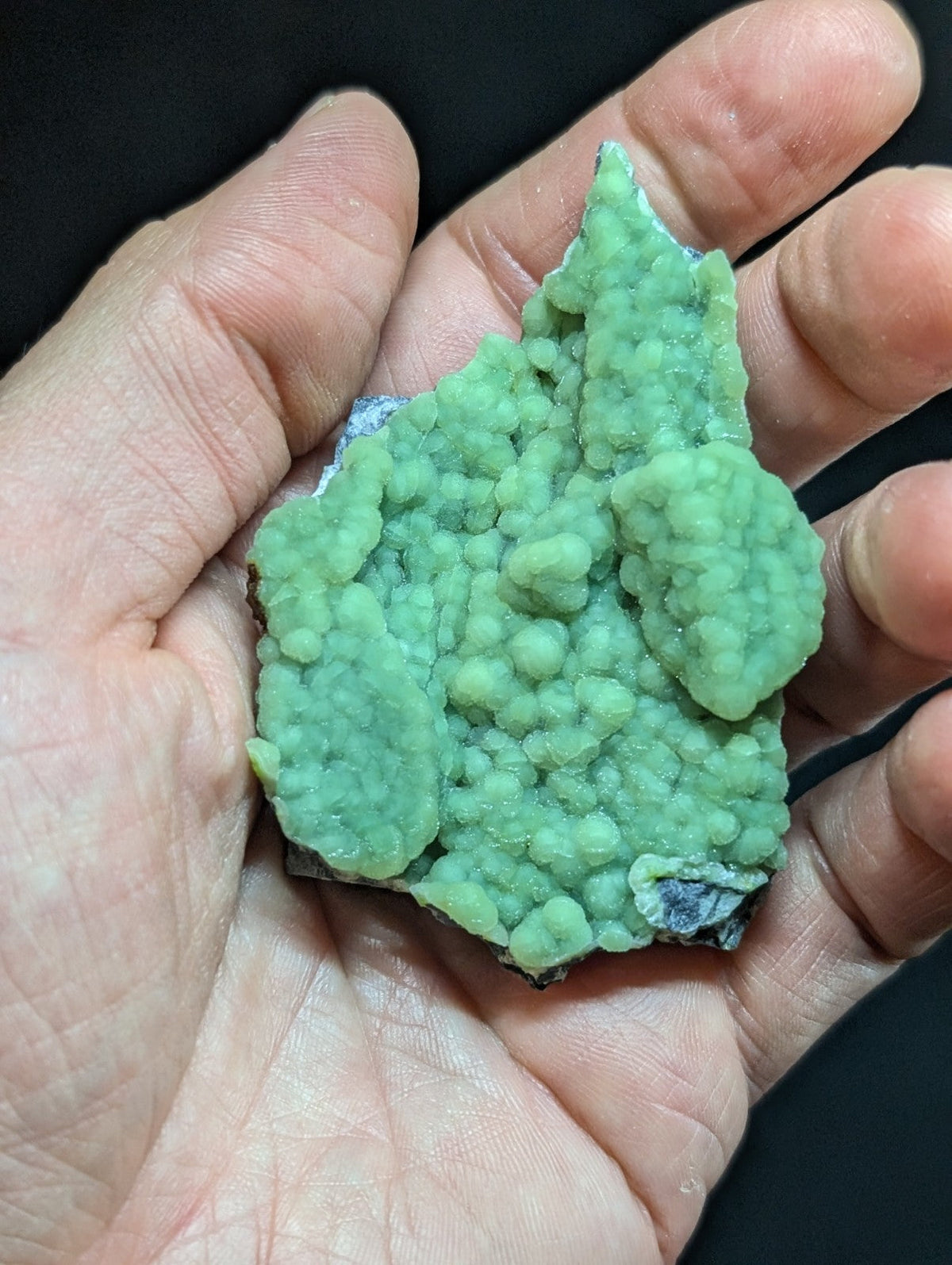 A vibrant green, textured mineral specimen with a bumpy, crystalline surface held in an open palm.