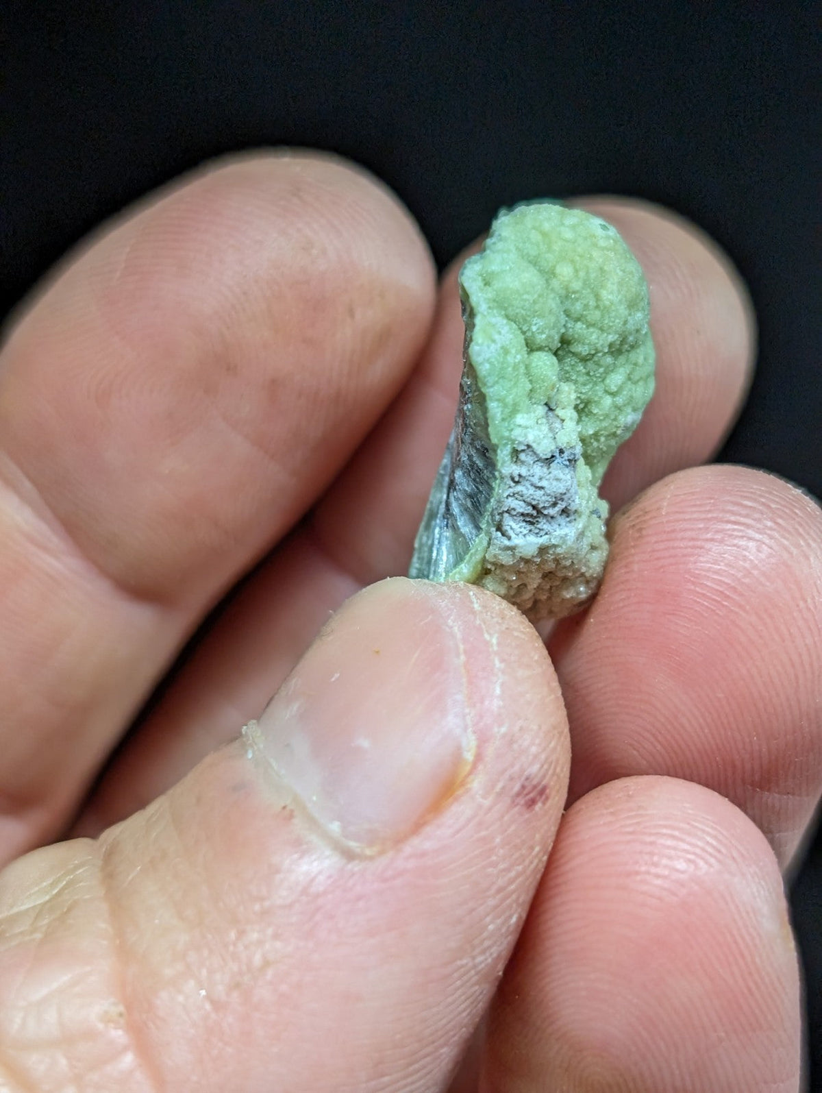 A rough, light green mineral specimen with a textured surface and some darker patches.