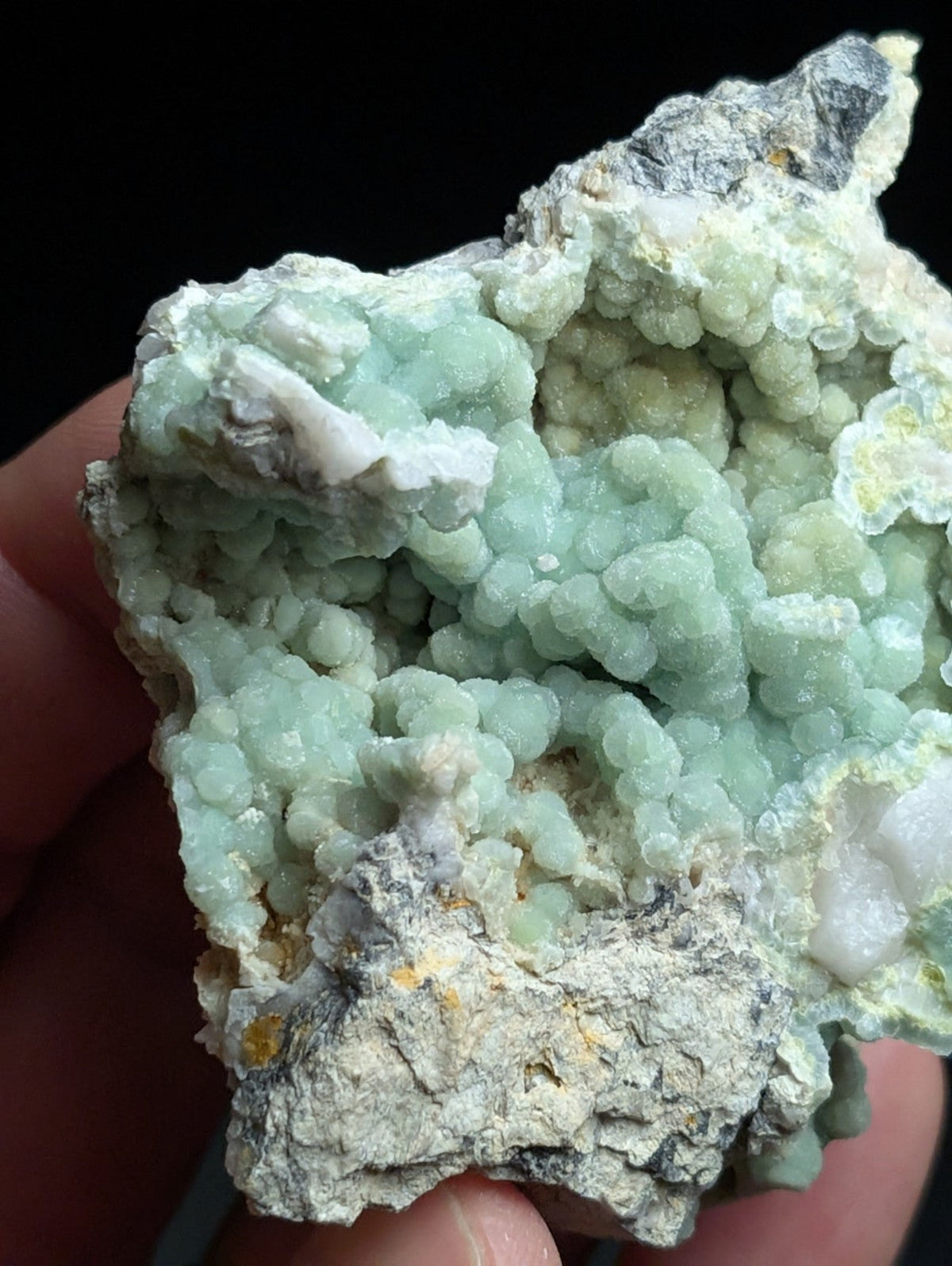 A pale green, crystalline mineral specimen with rounded, bubble-like formations and a rough, grayish matrix.