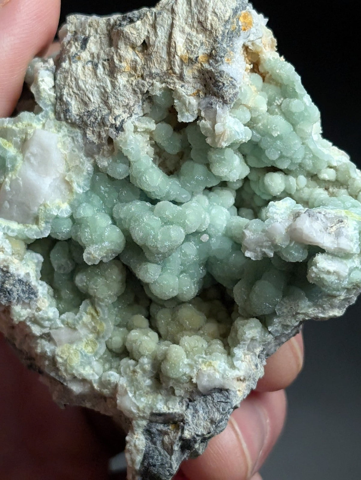 A cluster of pale green, bead-like crystals growing from a rough gray rock matrix.