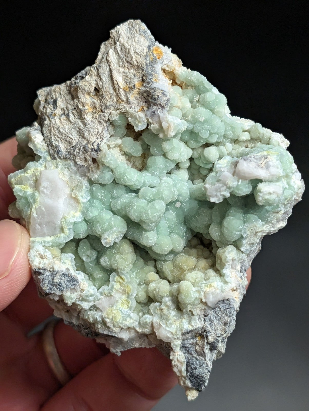 A hand holds a striking light green, bubbly mineral specimen with white and gray matrix rock.