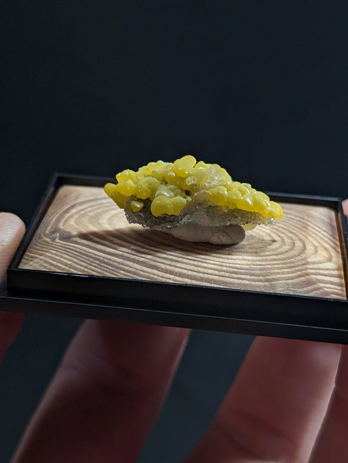 A vibrant yellow, crystalline mineral specimen with a textured, bumpy surface rests on a natural wood display base.