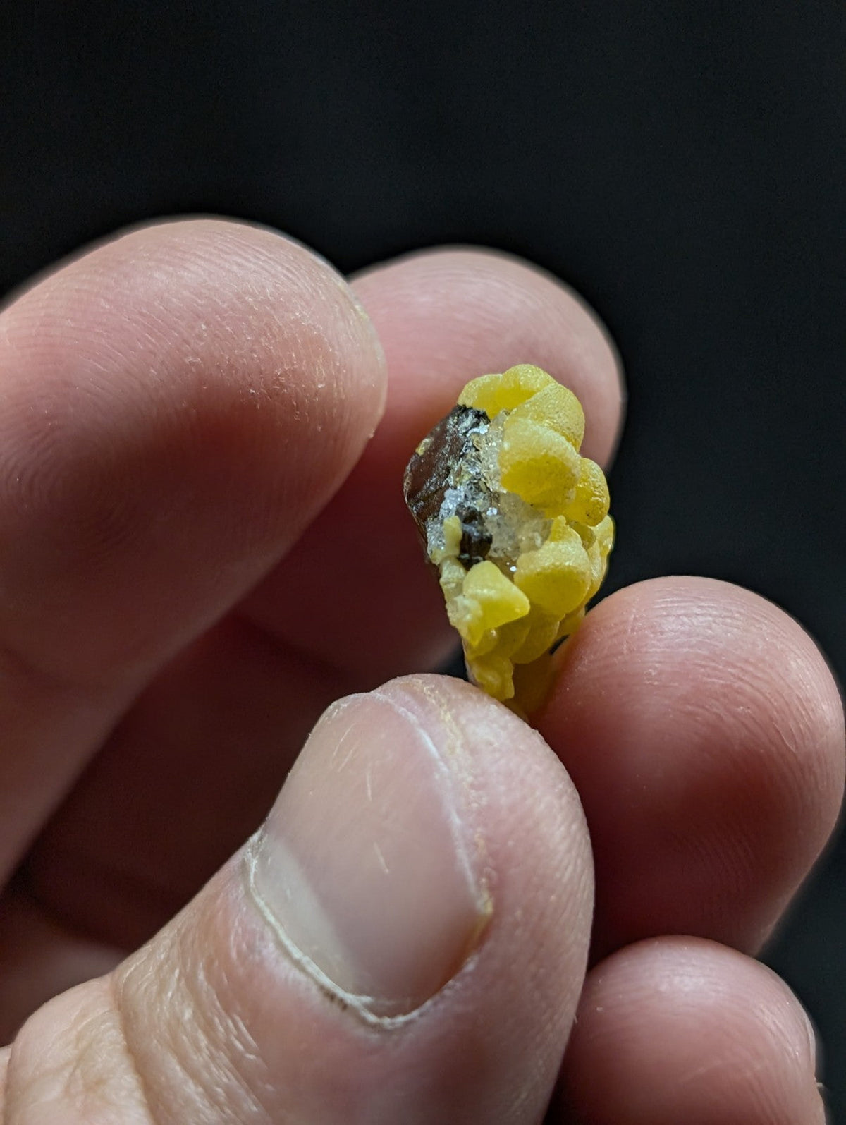 A small, irregularly shaped yellow mineral specimen with a dark, rough-textured patch on one side.