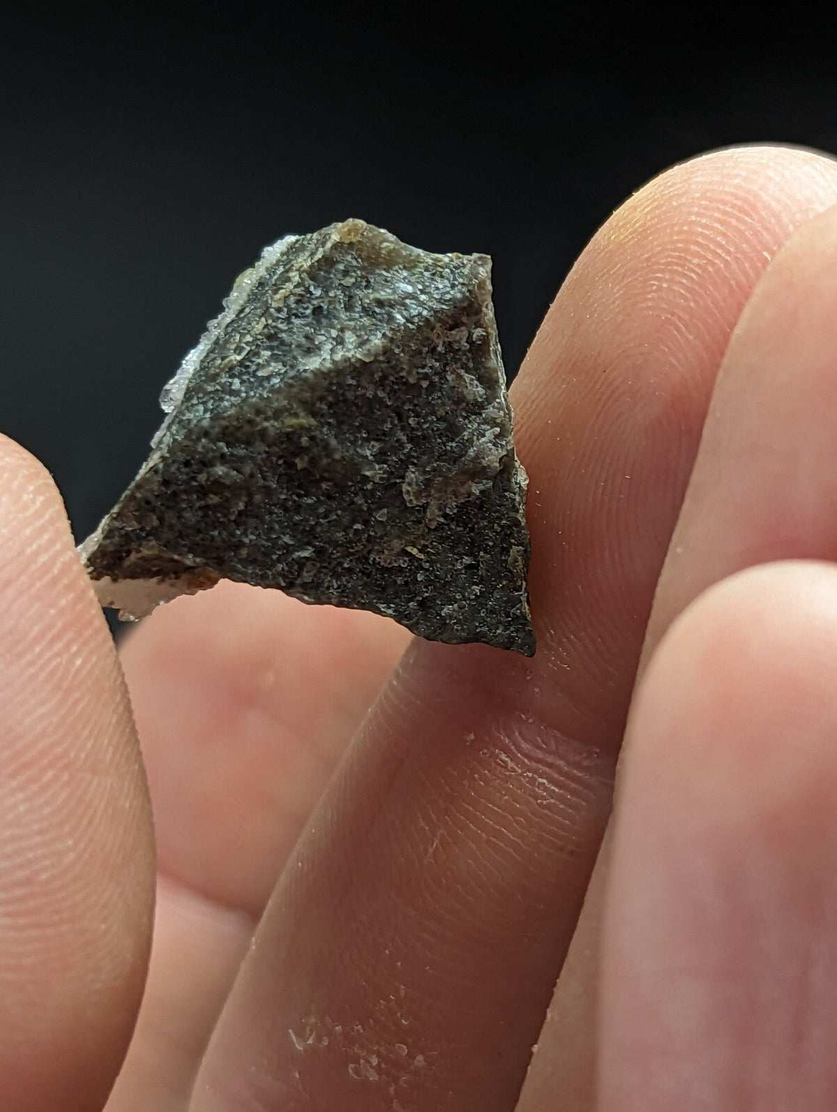 A rough, dark gray mineral fragment with a textured surface and irregular edges.