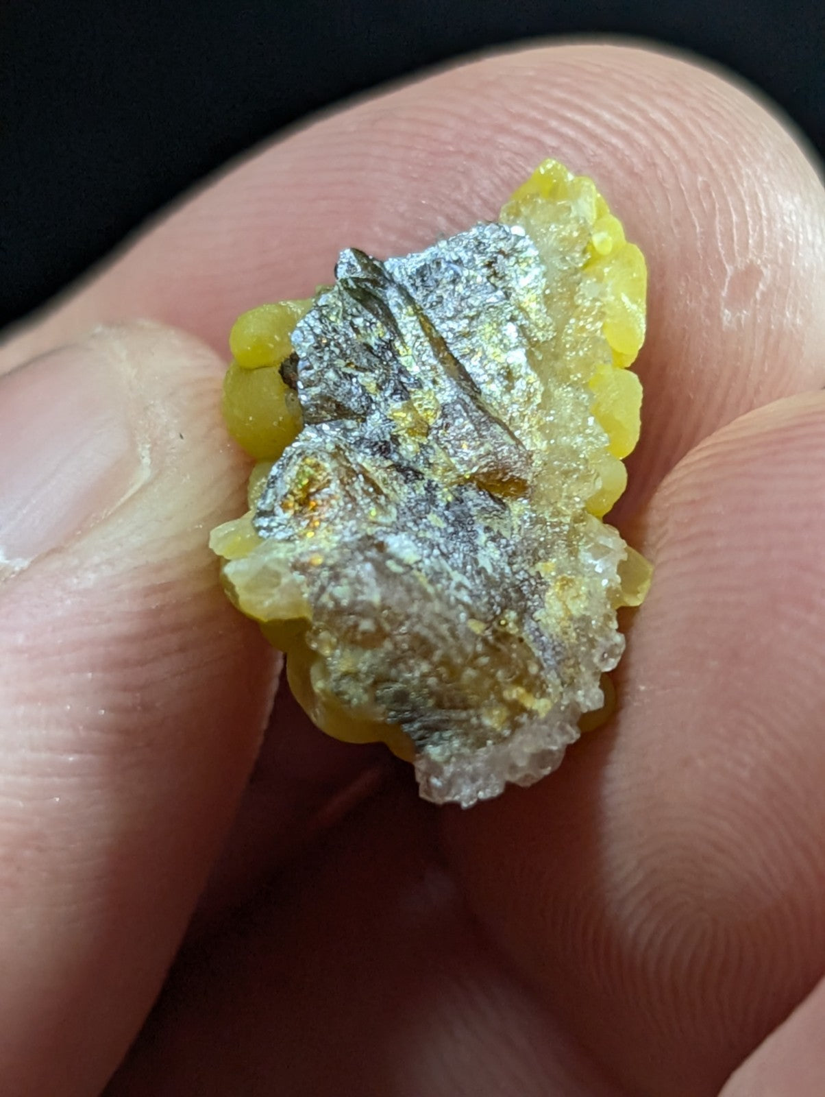A textured, irregularly shaped mineral specimen with a yellowish base and silver-gray metallic patches.