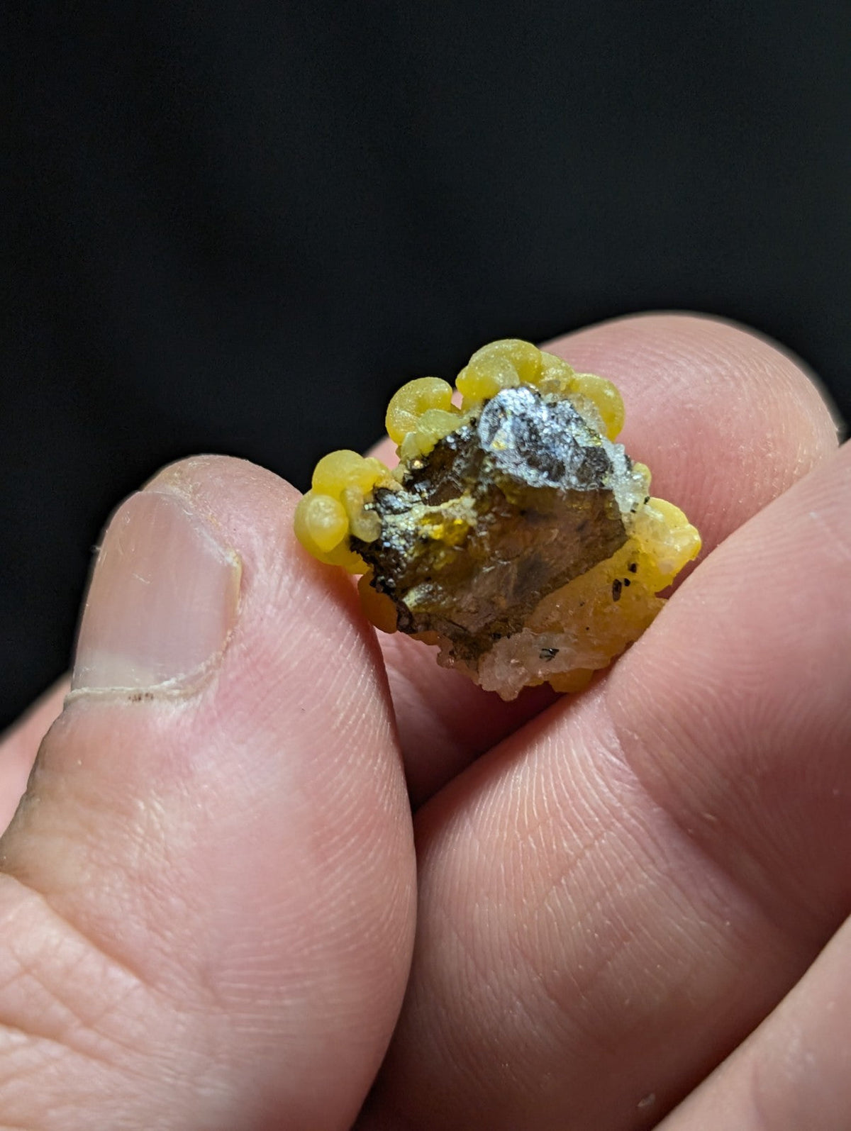 A yellow, bead-like mineral specimen with a rough, dark core and crystalline formations.