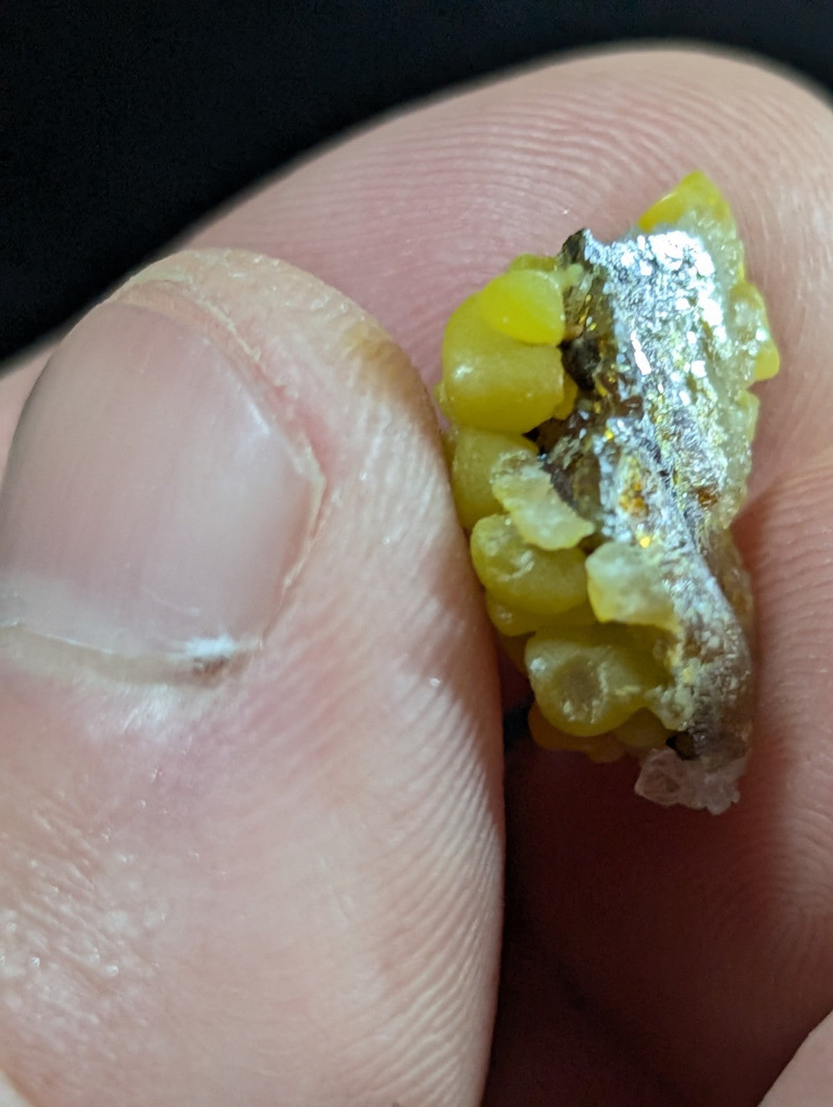 A chunky, irregularly shaped piece of yellowish-green mineral with a metallic silver sheen and visible gold flecks.