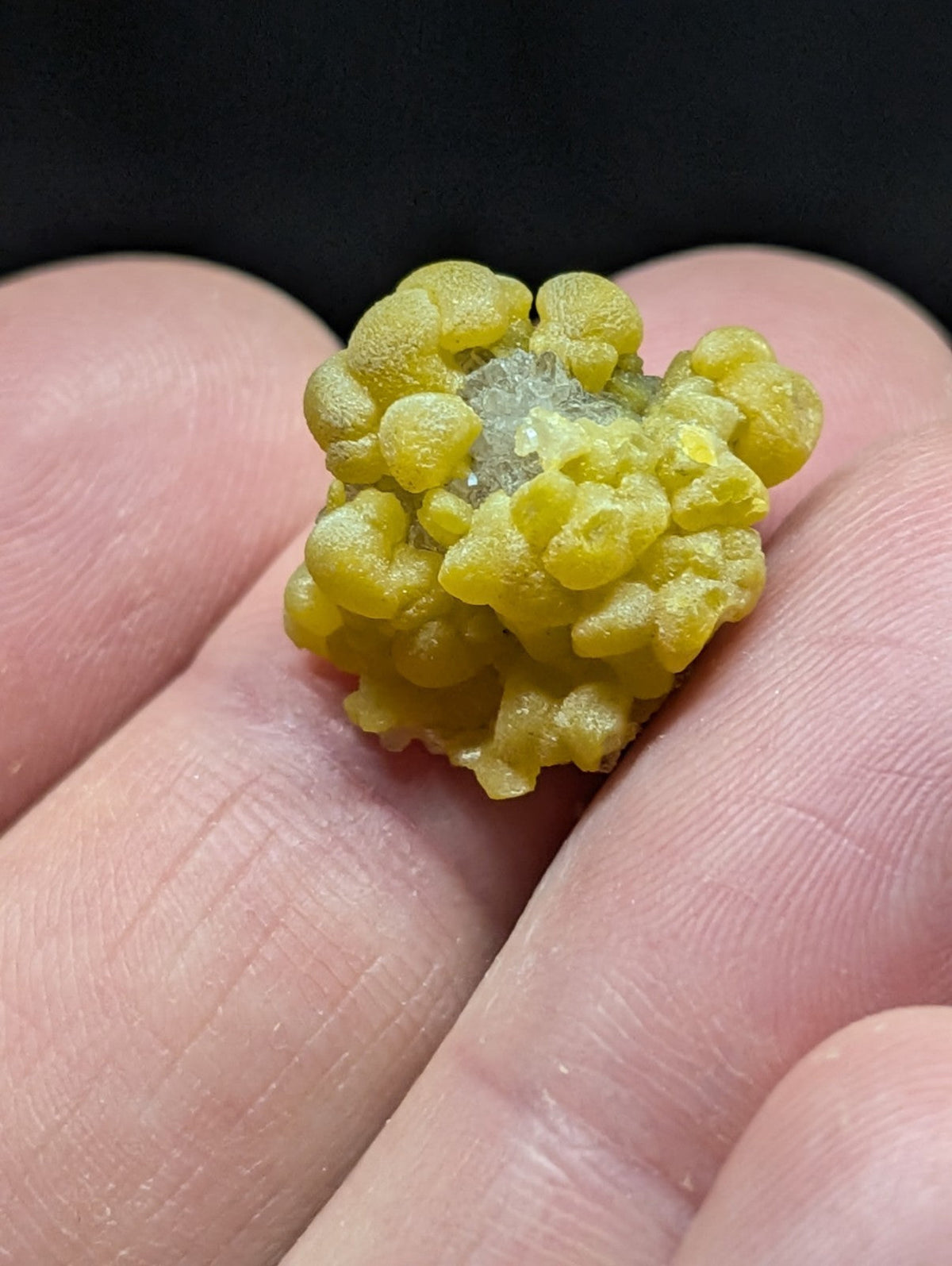 A vibrant yellow, bumpy mineral specimen with a crystalline center held in the palm.