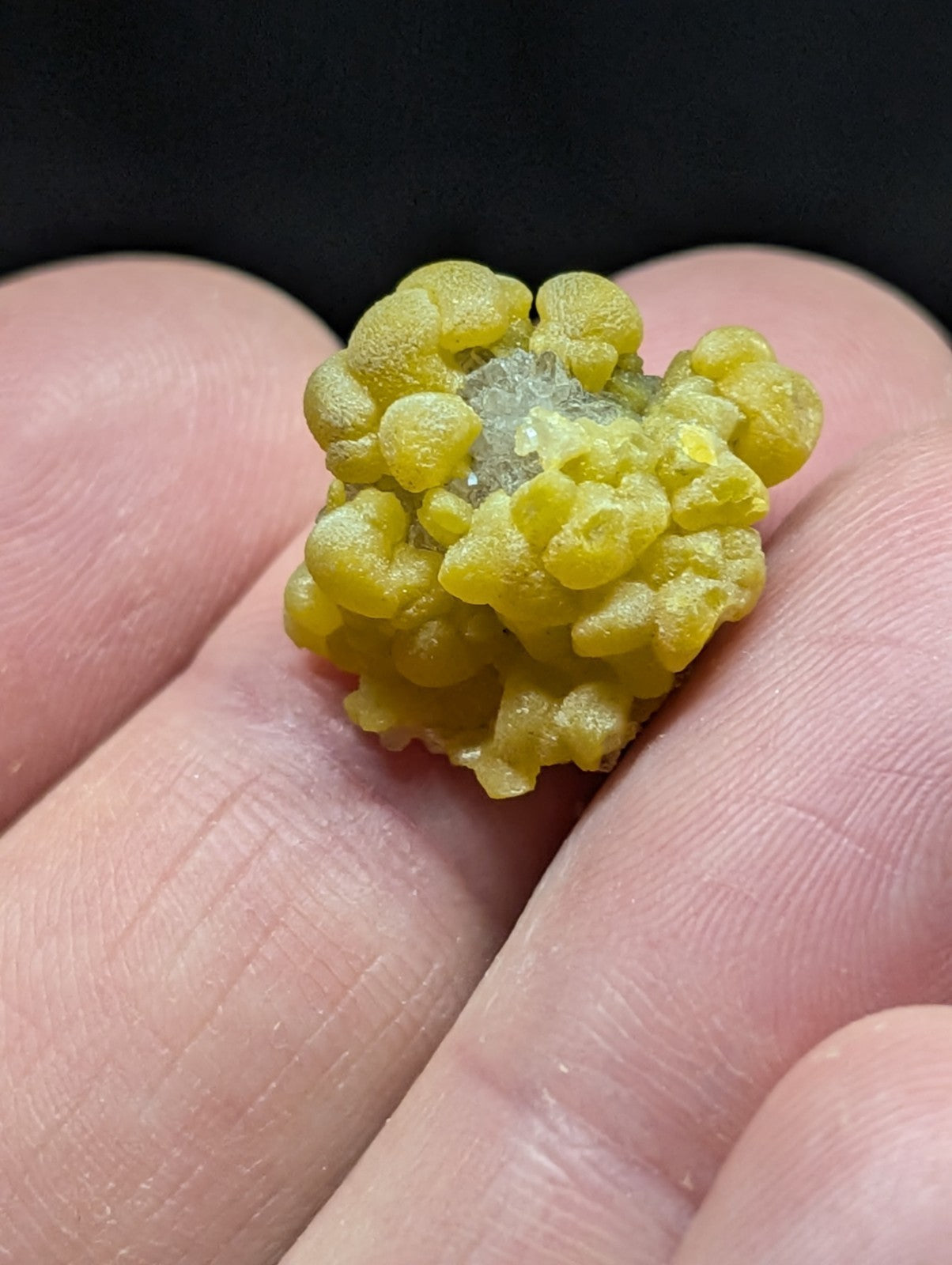 A vibrant yellow, bumpy mineral specimen with a crystalline center held in the palm.