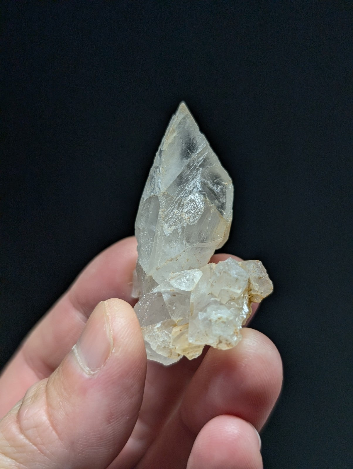 A translucent, pale quartz crystal cluster with a pointed tip and rougher base held gently in someone’s hand.