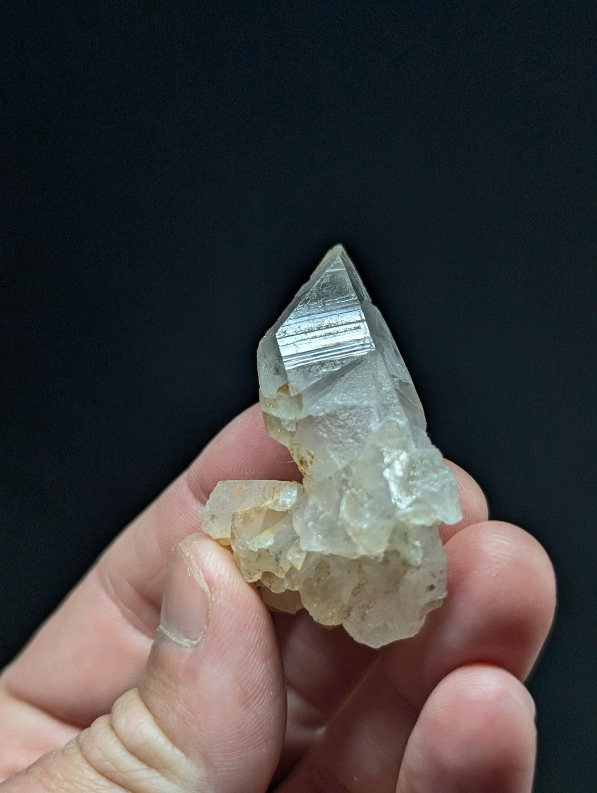 A translucent, pale quartz crystal cluster with a pointed tip and striated facets.