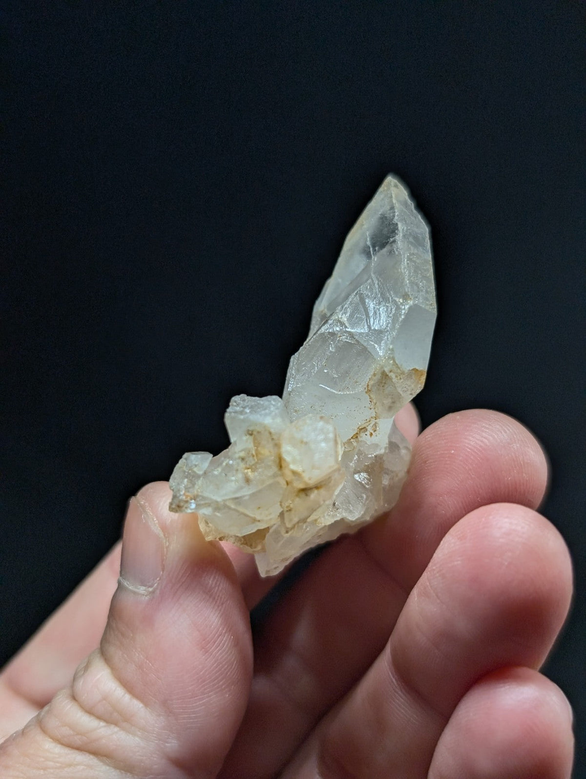 A translucent, pale quartz crystal cluster with a pointed tip and rougher base held gently in someone’s hand.