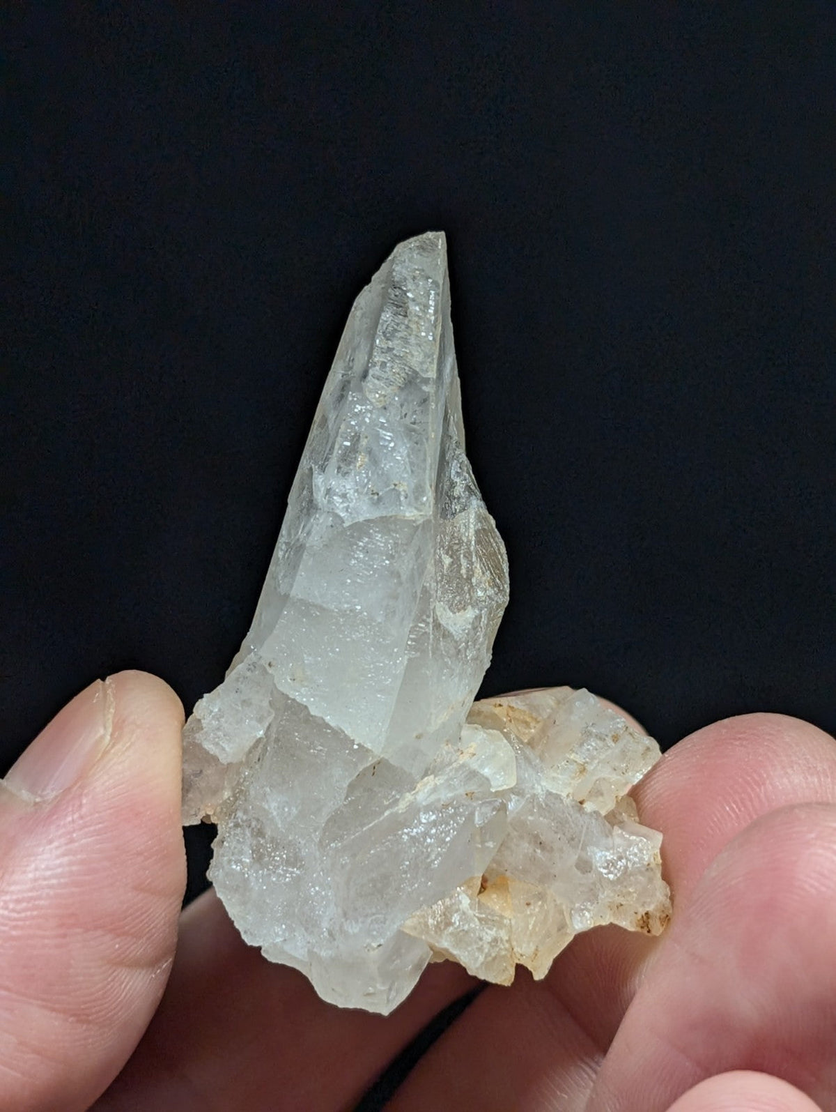 A translucent, clear quartz crystal cluster with a pointed tip and rough, faceted surfaces.