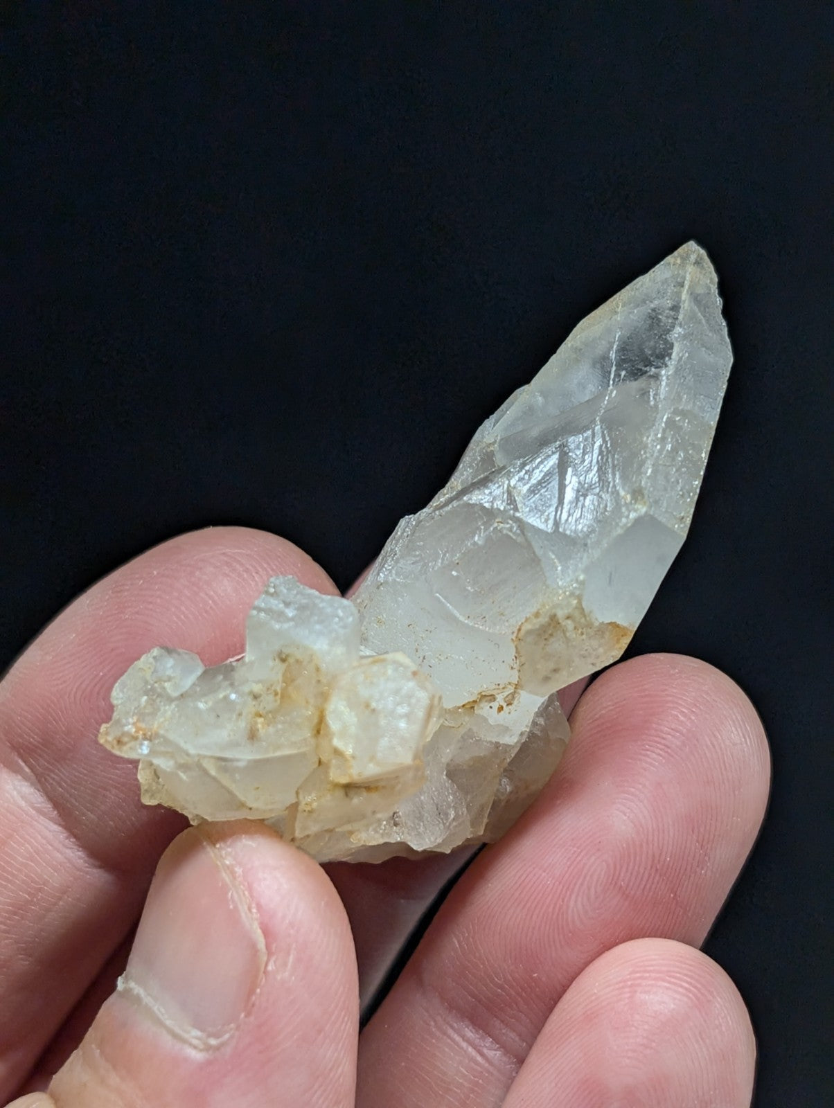 A translucent, pale quartz crystal cluster with a pointed tip and rougher base held gently in someone’s hand.