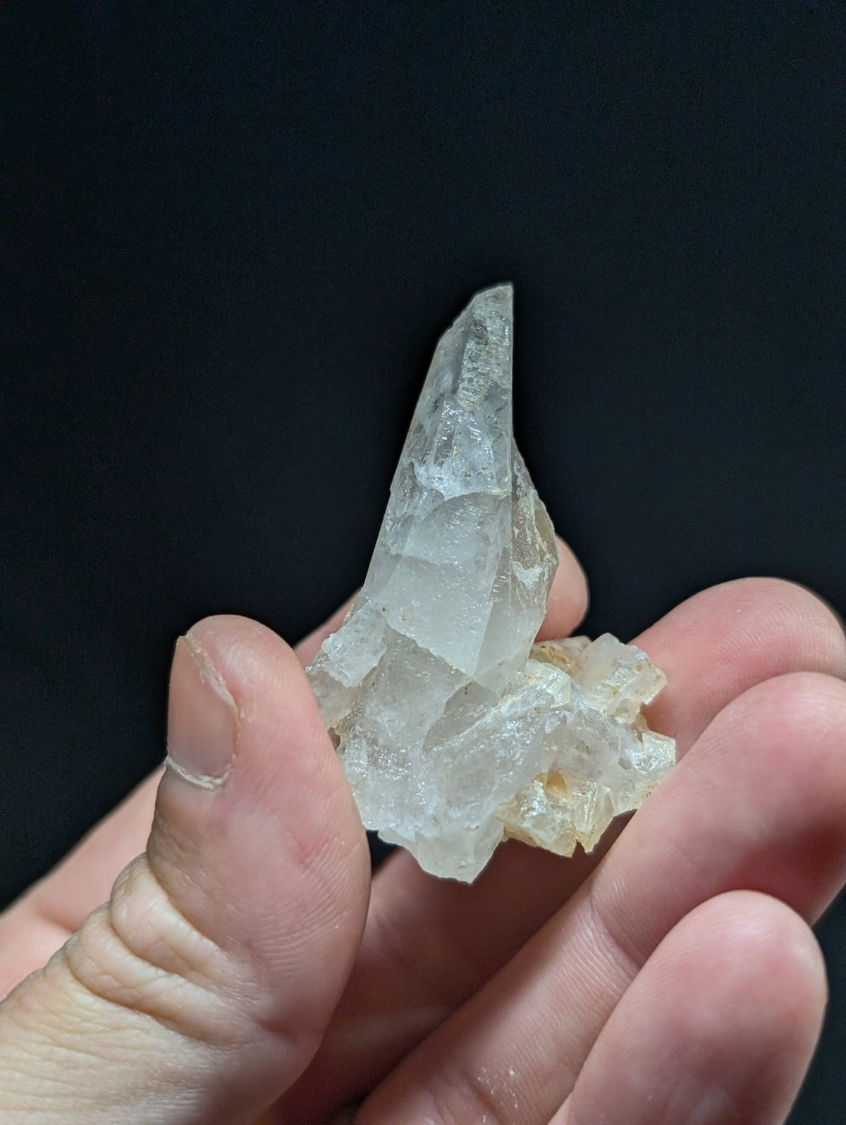 A translucent, clear quartz crystal cluster with a pointed tip and rough, faceted surfaces.